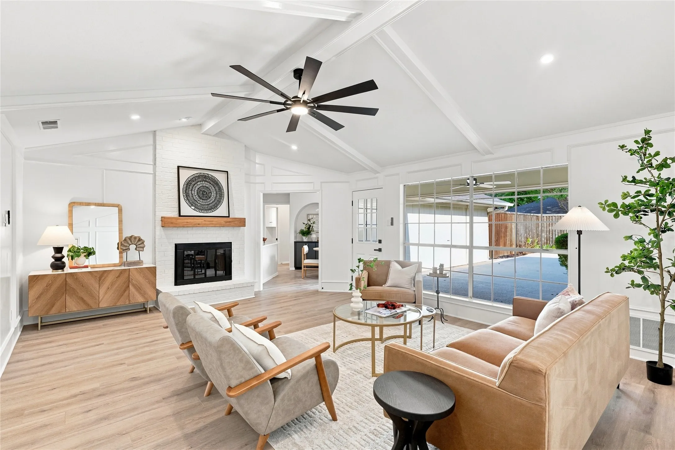 Vaulted ceiling with exposed beams, brick fireplace with wood mantel, large pane windows, wood-finish flooring, and recessed lighting