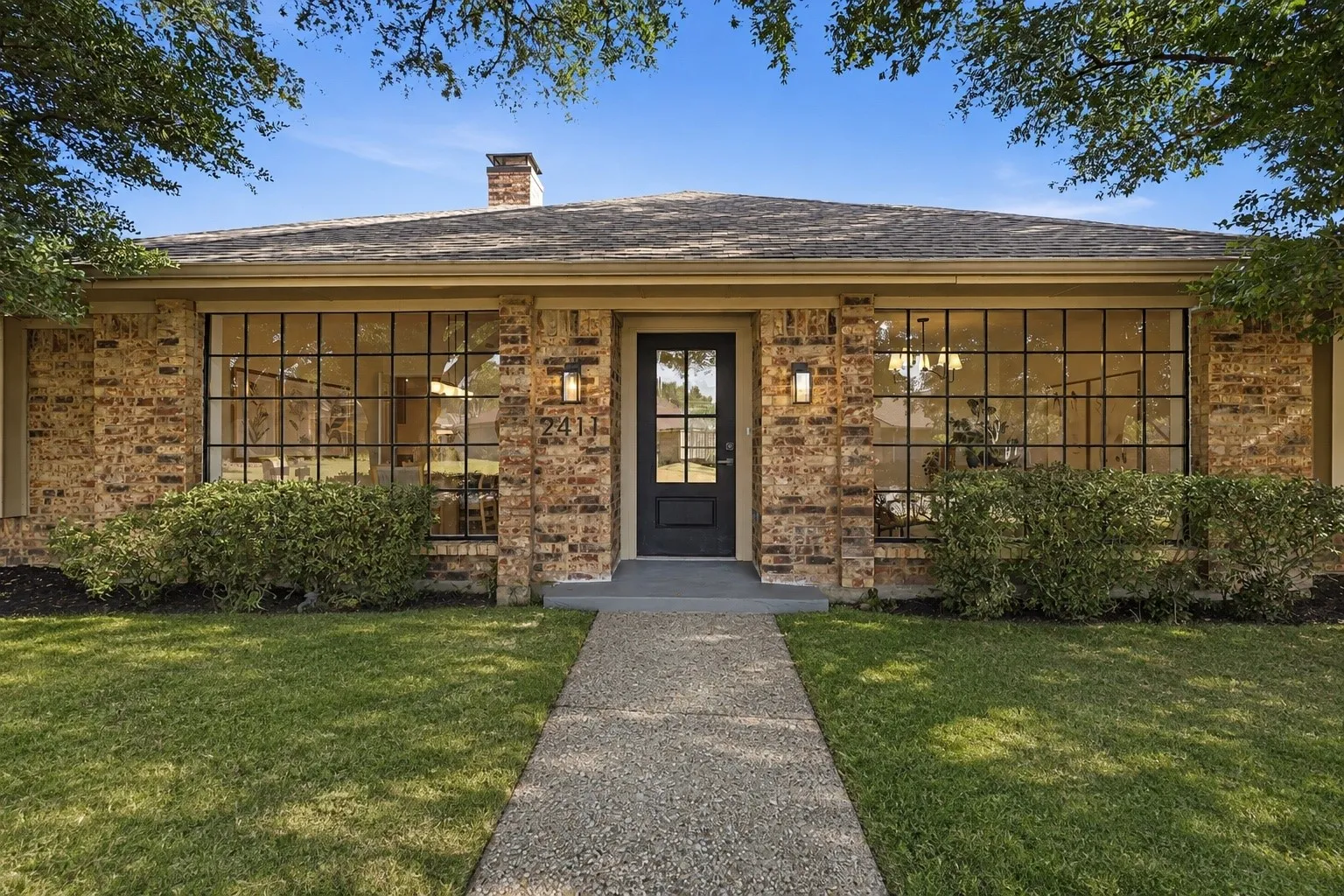 Brick facade with extensive grid-pattern windows, a black entry door, and a shingle roof