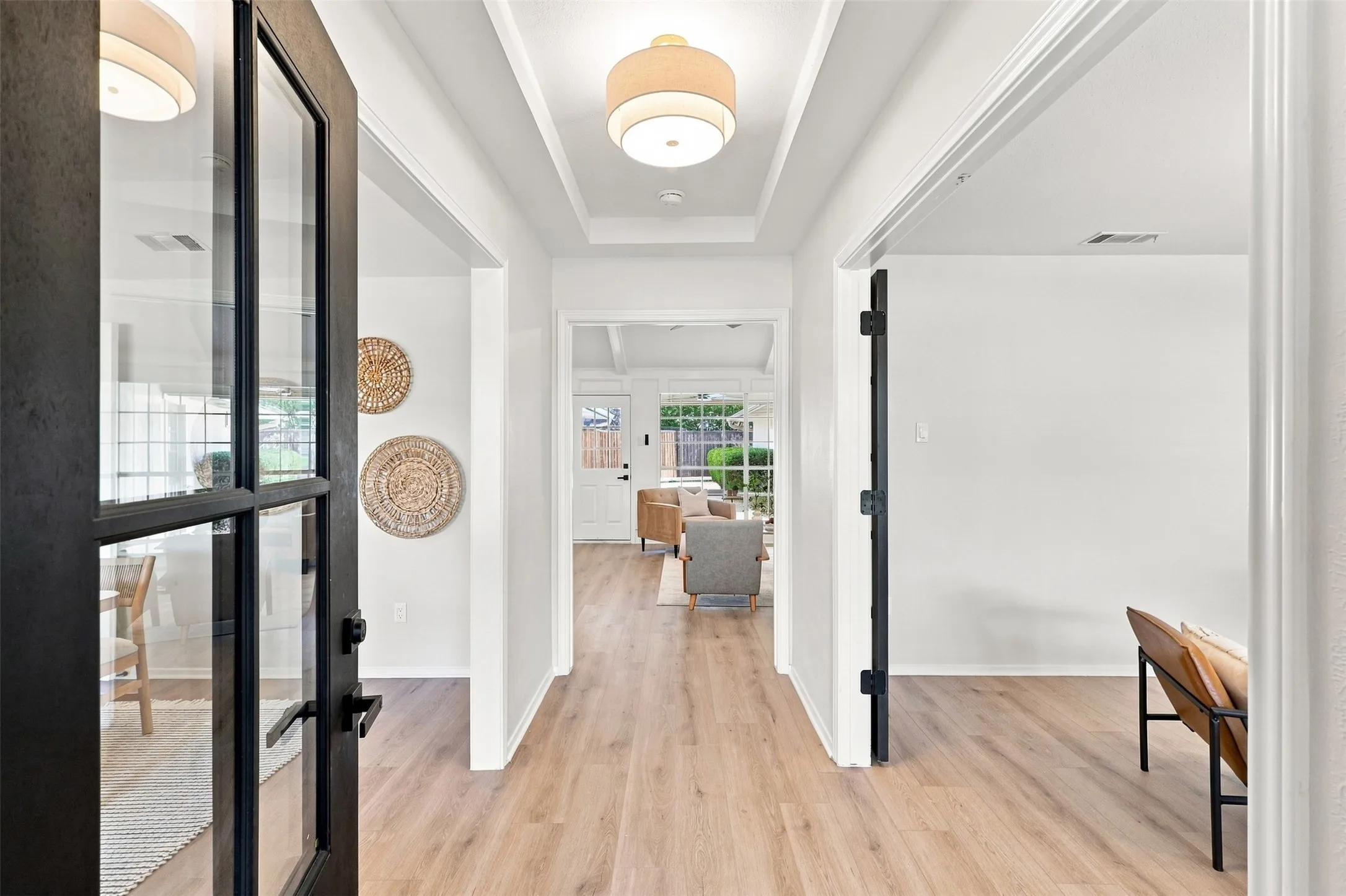 Light wood-finish flooring extending throughout, coffered ceiling, recessed lighting, and a black-framed glass panel door
