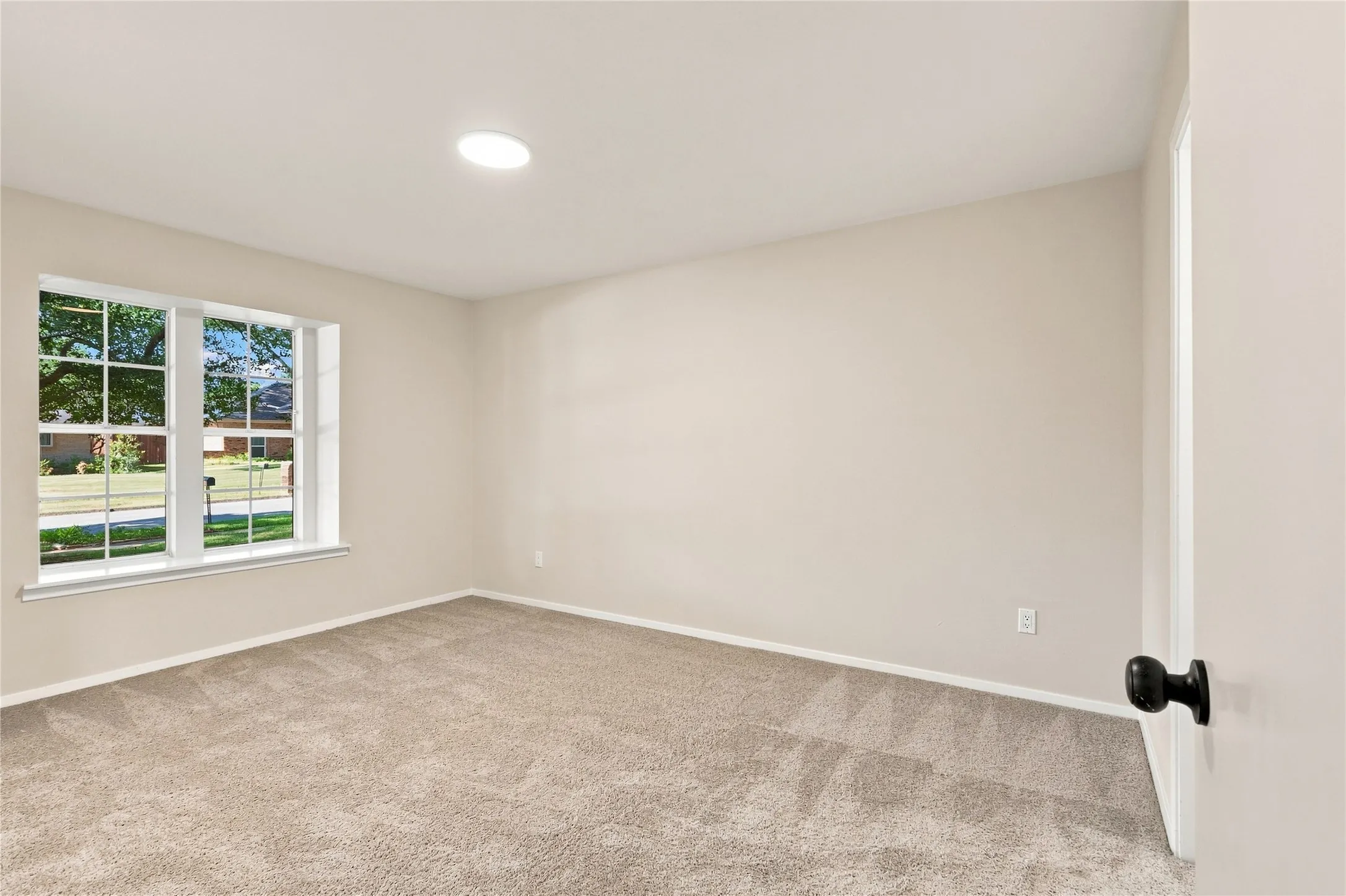 Neutral-toned wall paint, recessed ceiling lighting, light-colored carpeting, white window trim, and a black doorknob