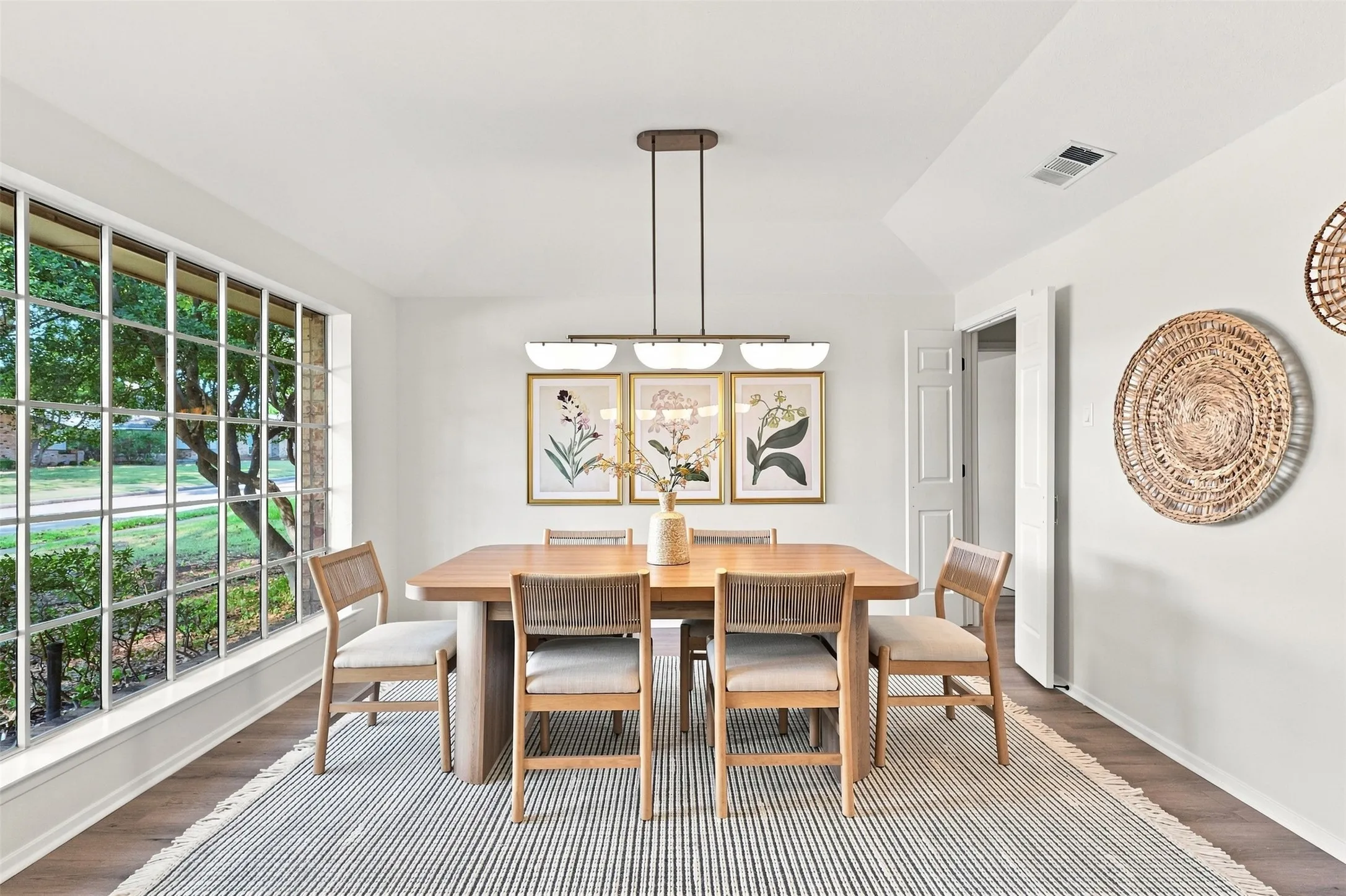 Bright dining room anchored by a wood-finish table and chairs, illuminated by a linear pendant fixture