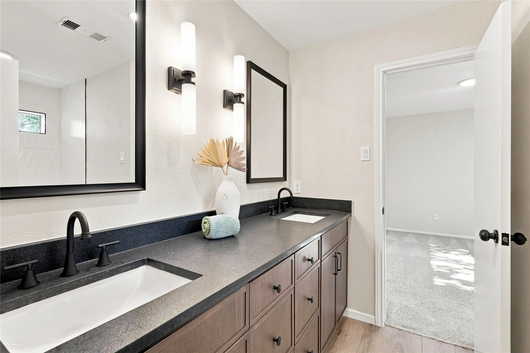 Dual sink vanity with dark wood-finish cabinetry, black countertops, and matte black fixtures