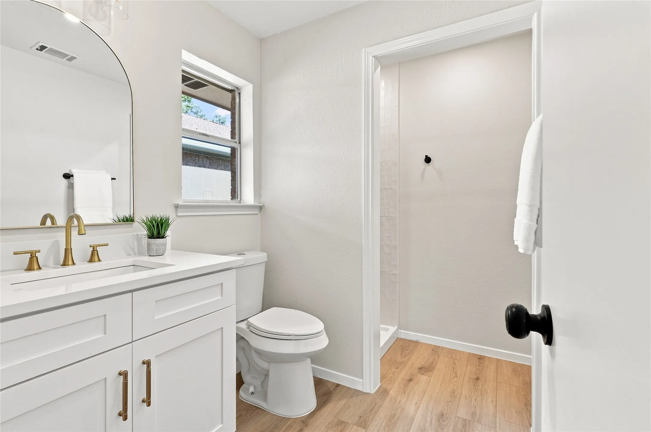 White vanity with gold-finish fixtures and hardware, rectangular undermount sink, and a framed arched mirror