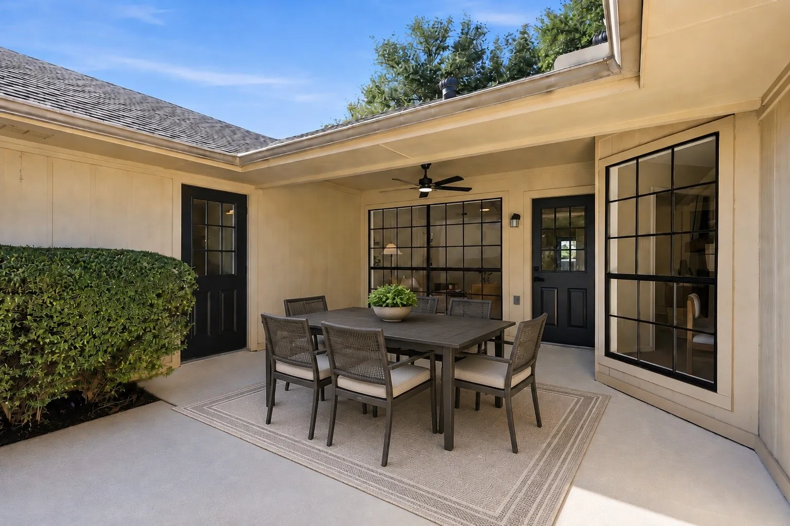 Covered patio with concrete flooring, integrated ceiling fan, and multiple exterior doors with glass panels