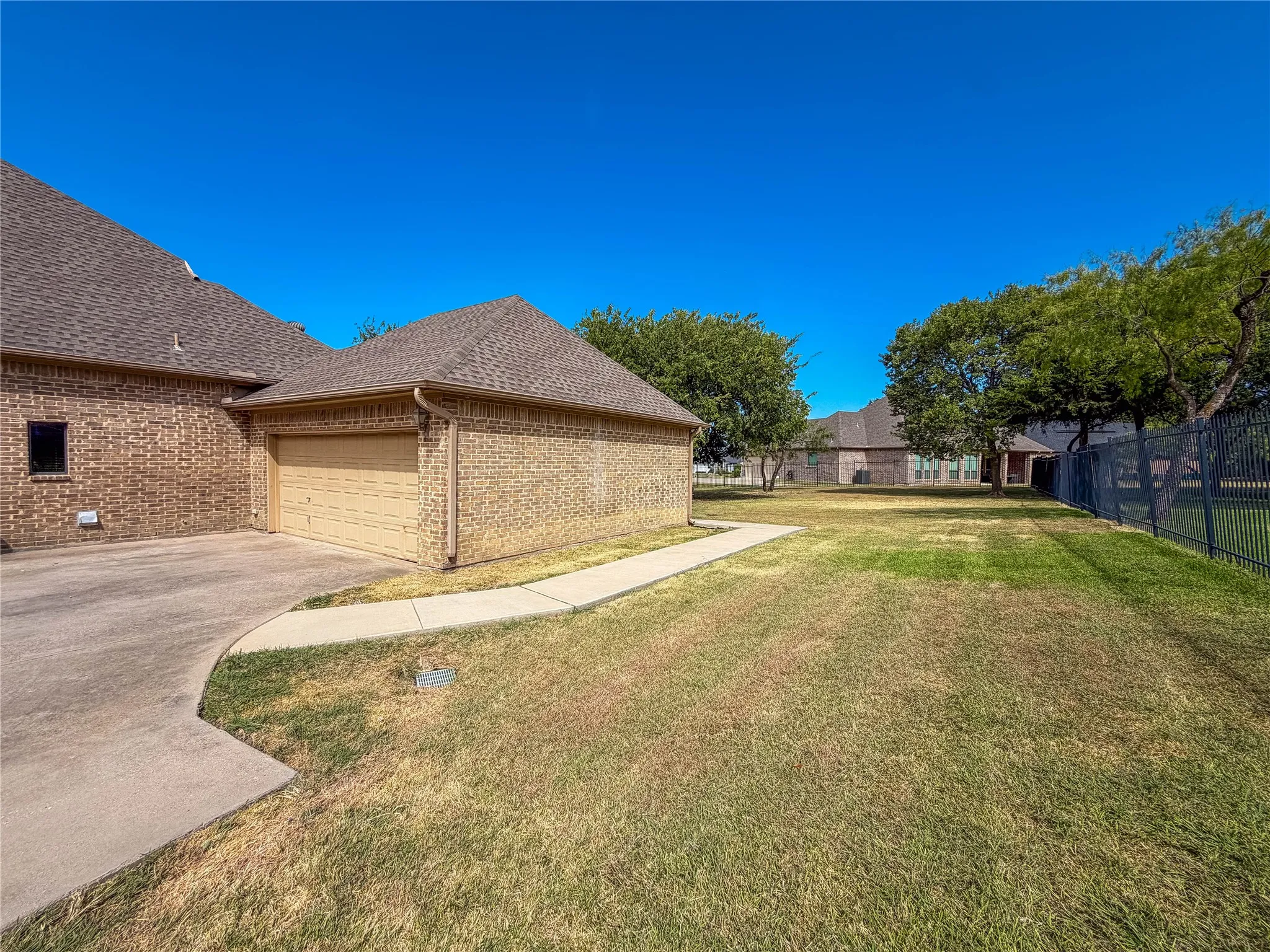 Brick exterior with a detached garage, concrete driveway, and mature landscaping