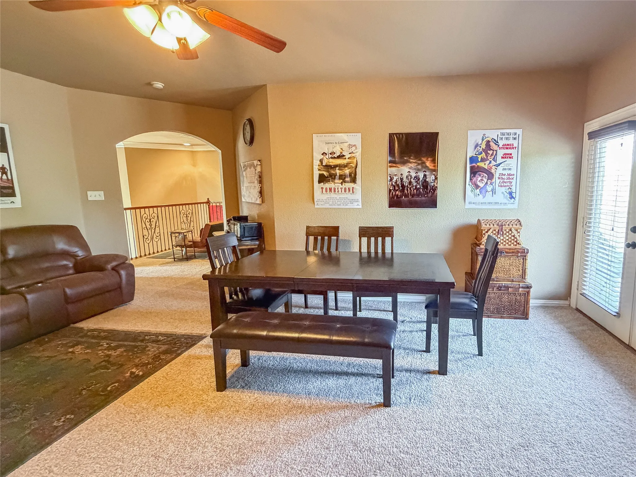 Expansive carpeted living area with a ceiling fan, arched doorway, and built-in railing