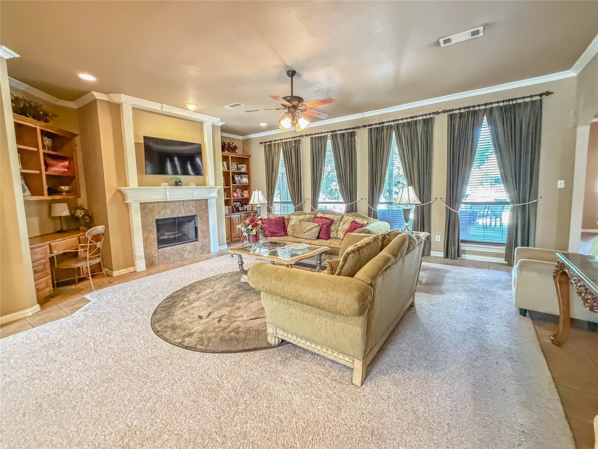 Spacious living area featuring a tile-surround fireplace with a mantel, built-in shelving, crown molding, and multiple windows