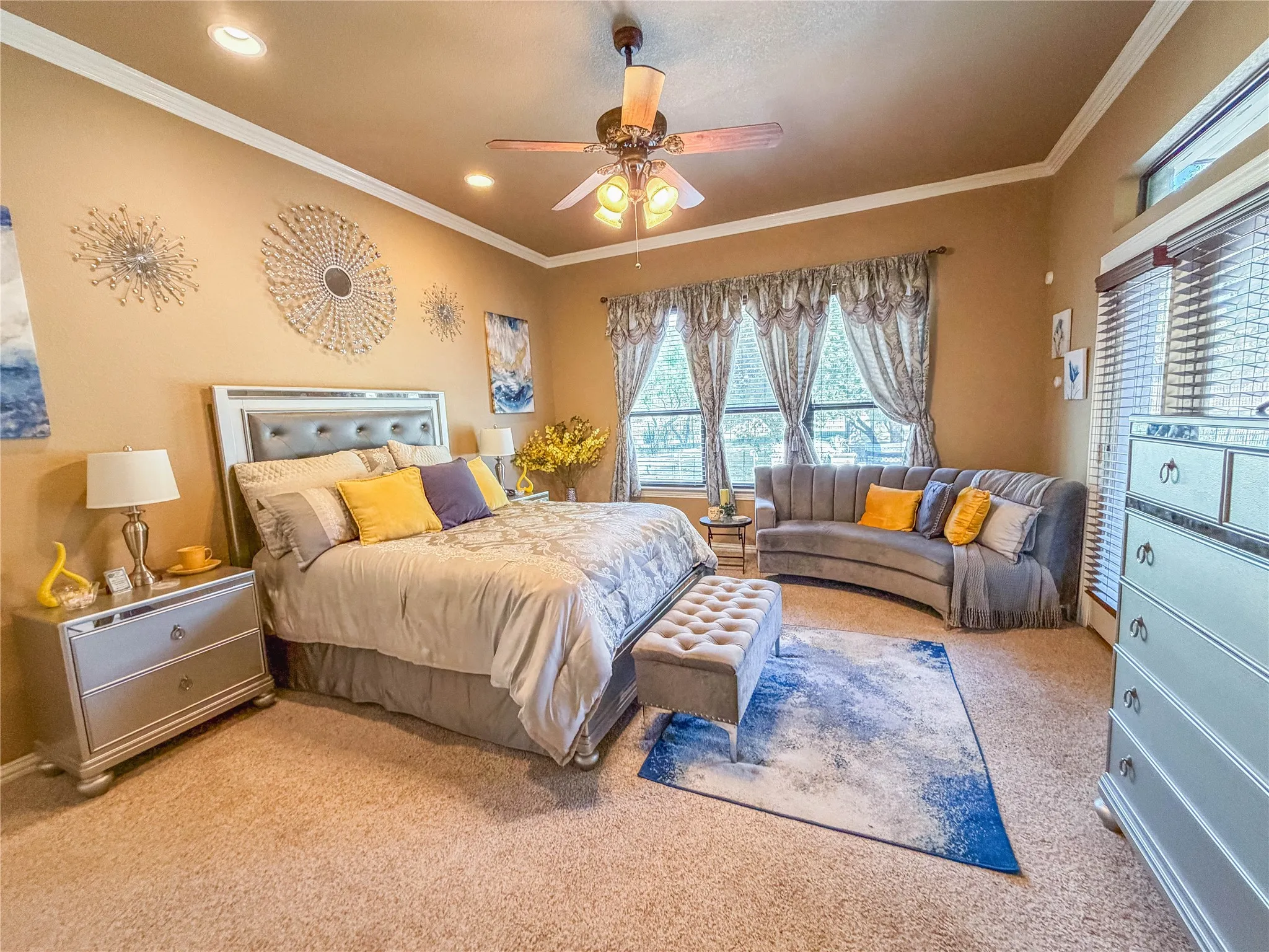 Tray ceiling with crown molding, ceiling fan with integrated lighting, recessed lighting, carpeted flooring, and multiple windows
