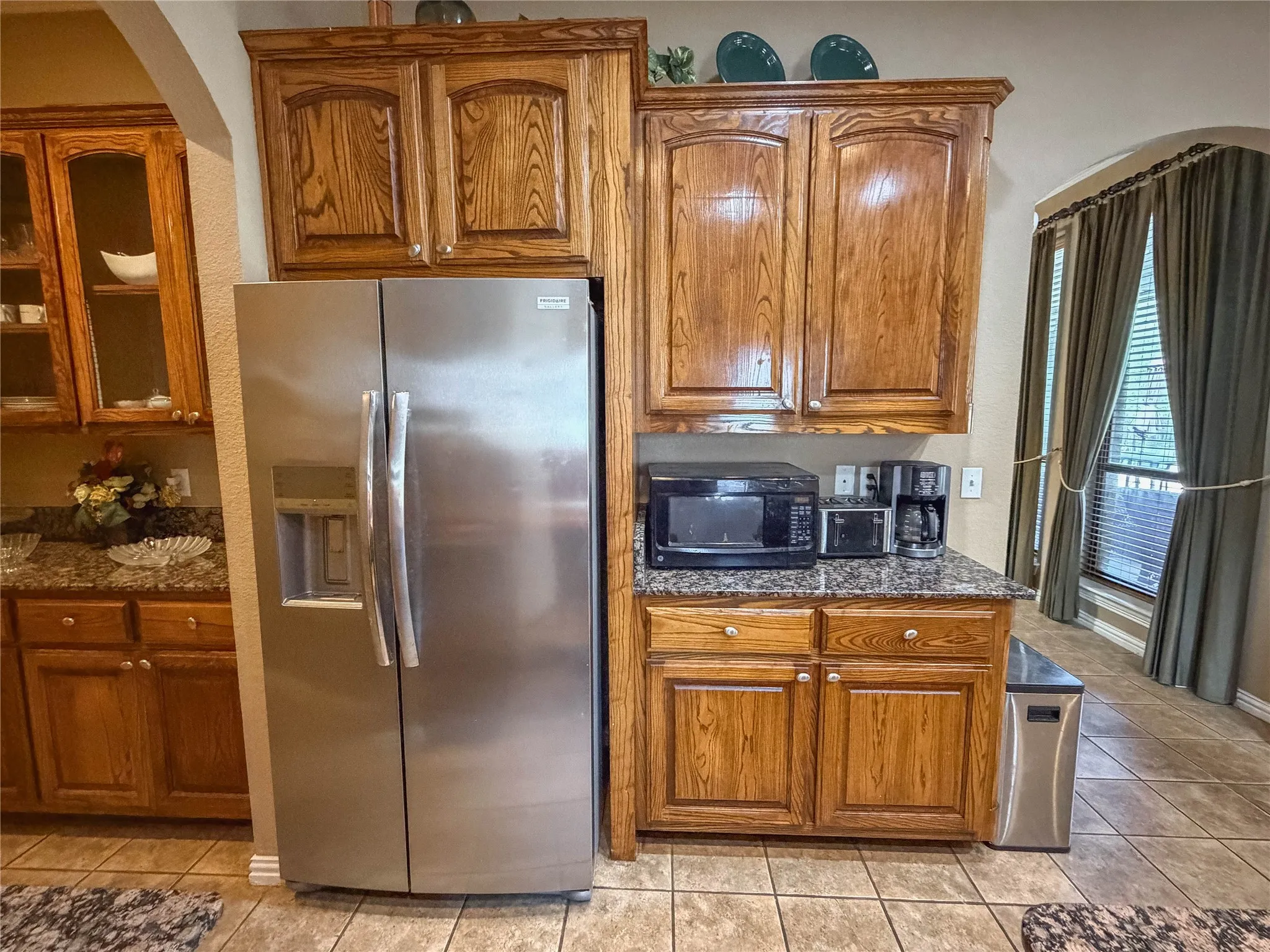 Solid wood cabinetry with panel doors, stainless steel side-by-side refrigerator, granite-style countertops, and ceramic tile flooring