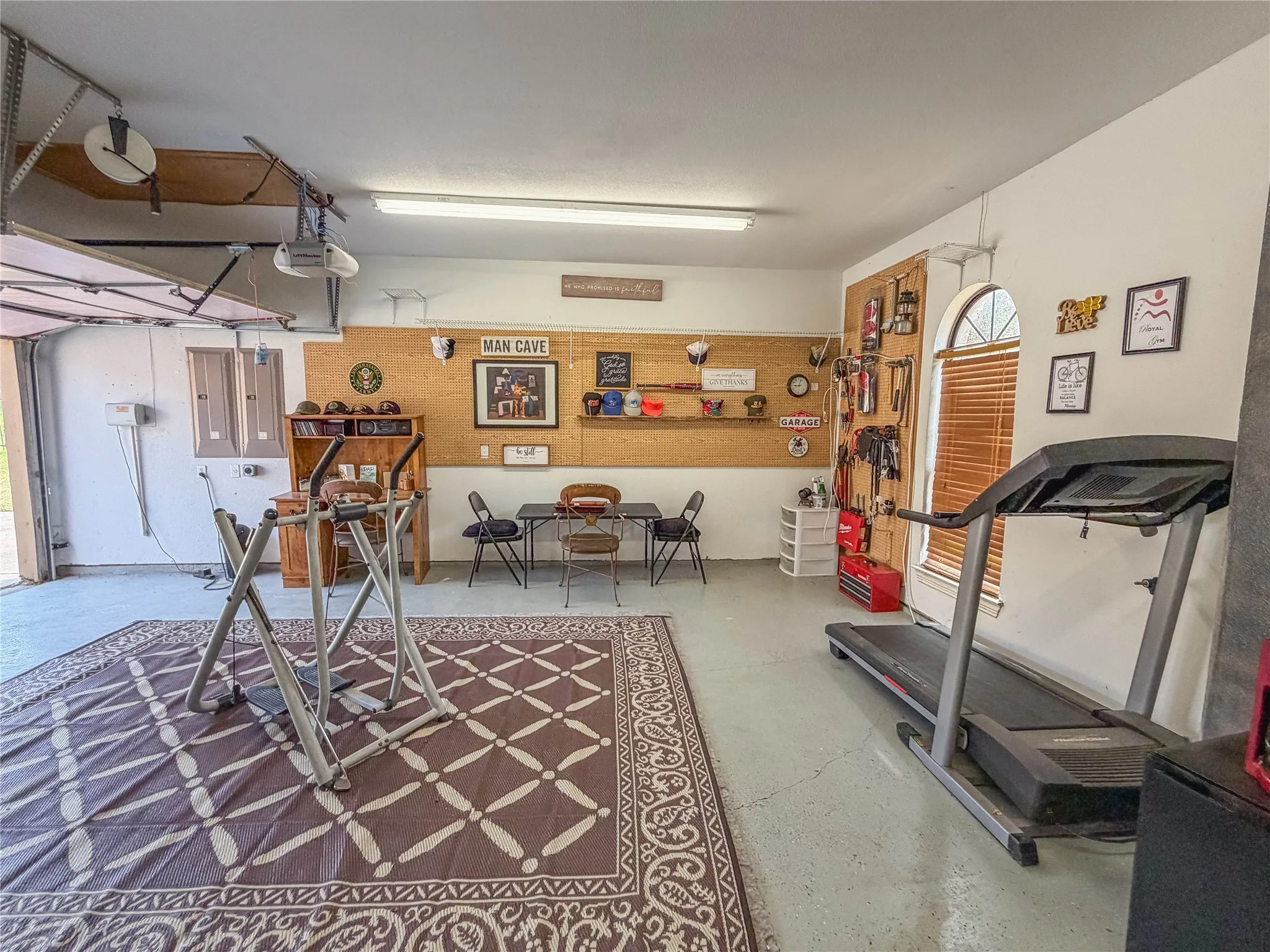 Garage space featuring a roll-up door, arched window with horizontal blinds, and a built-in cork board wall