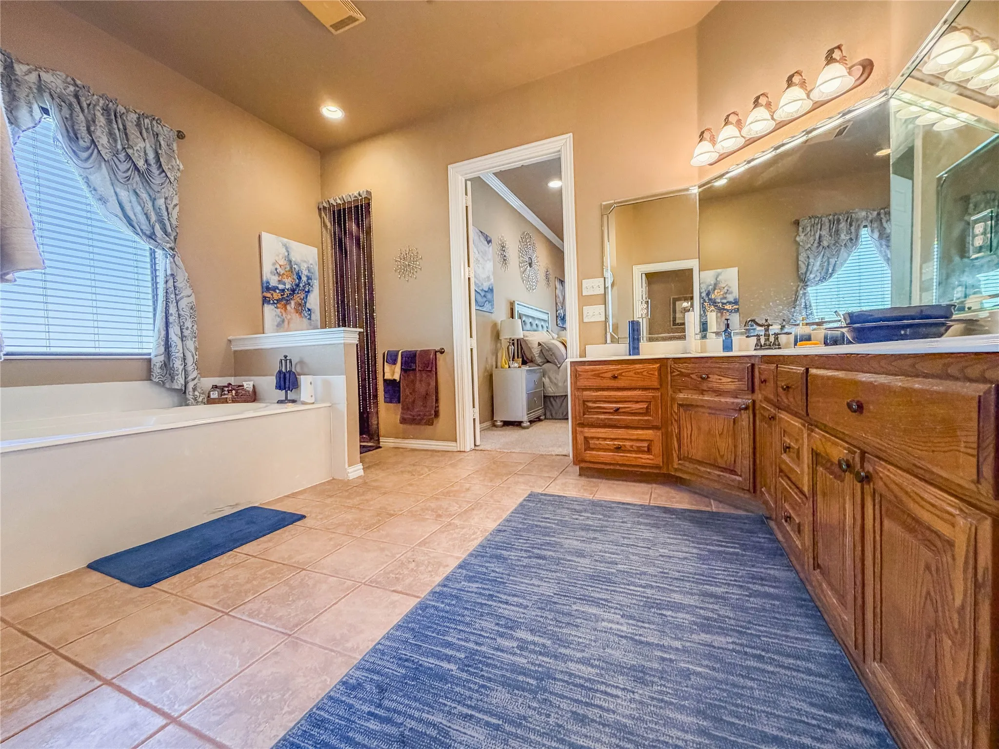 Soaking tub, dual vanity with wood-finish cabinetry, tile flooring, and integrated wall mirror