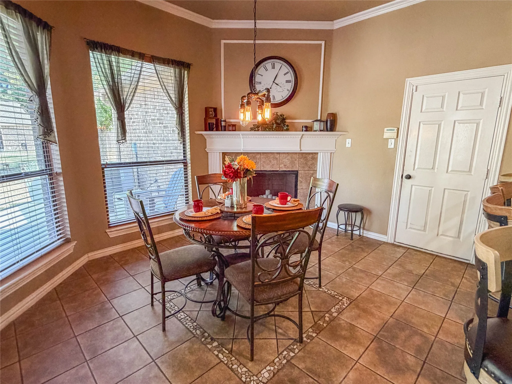 Tiled flooring with decorative inlay, corner fireplace with tile surround, white mantel, and crown molding
