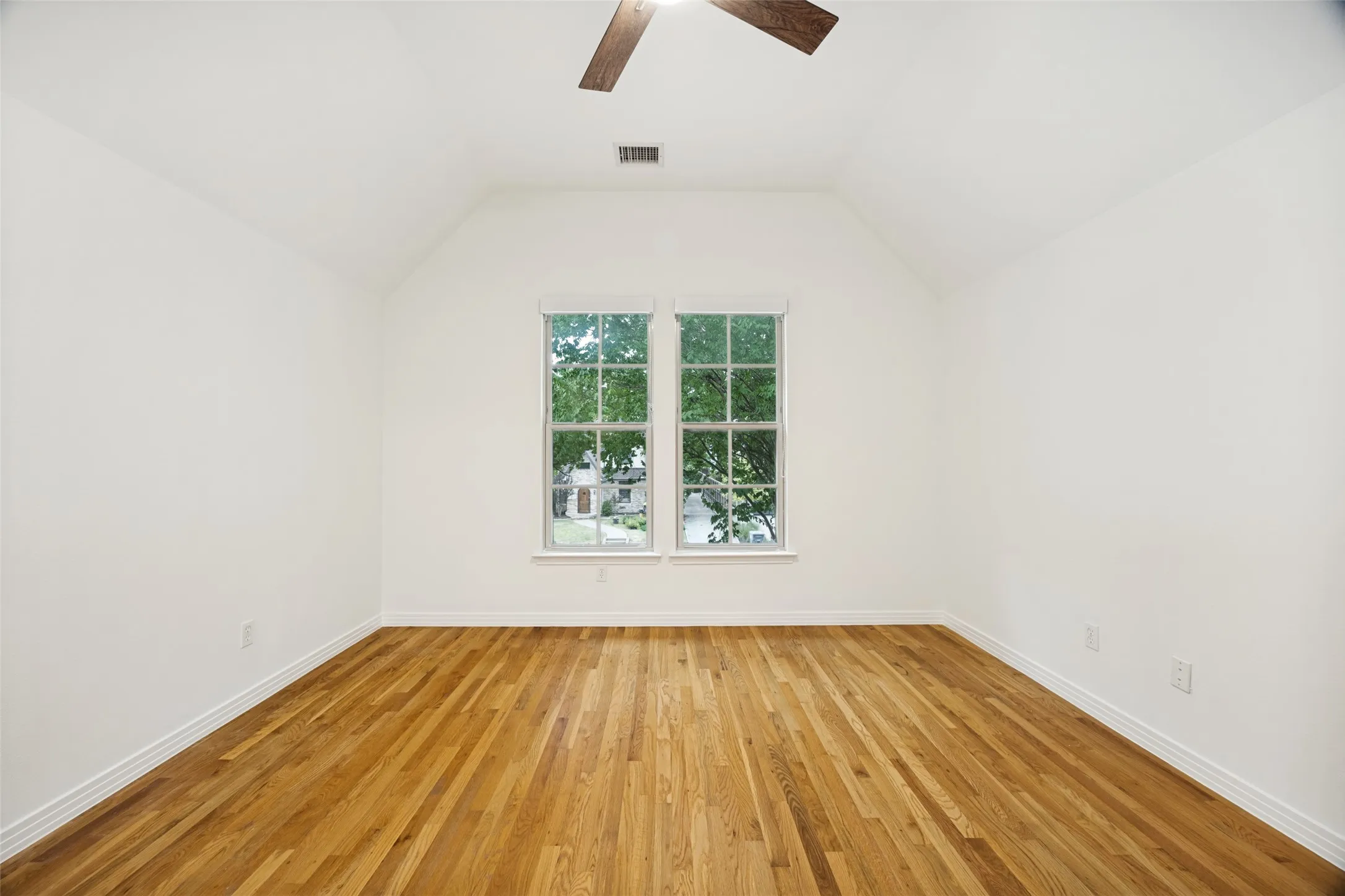 Upstairs secondary bedroom with hardwood floors and vaulted ceiling