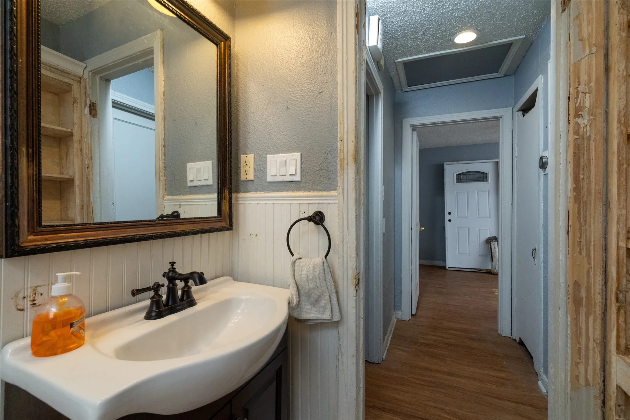 Pedestal sink with dark-toned fixtures, framed mirror, and beadboard paneling