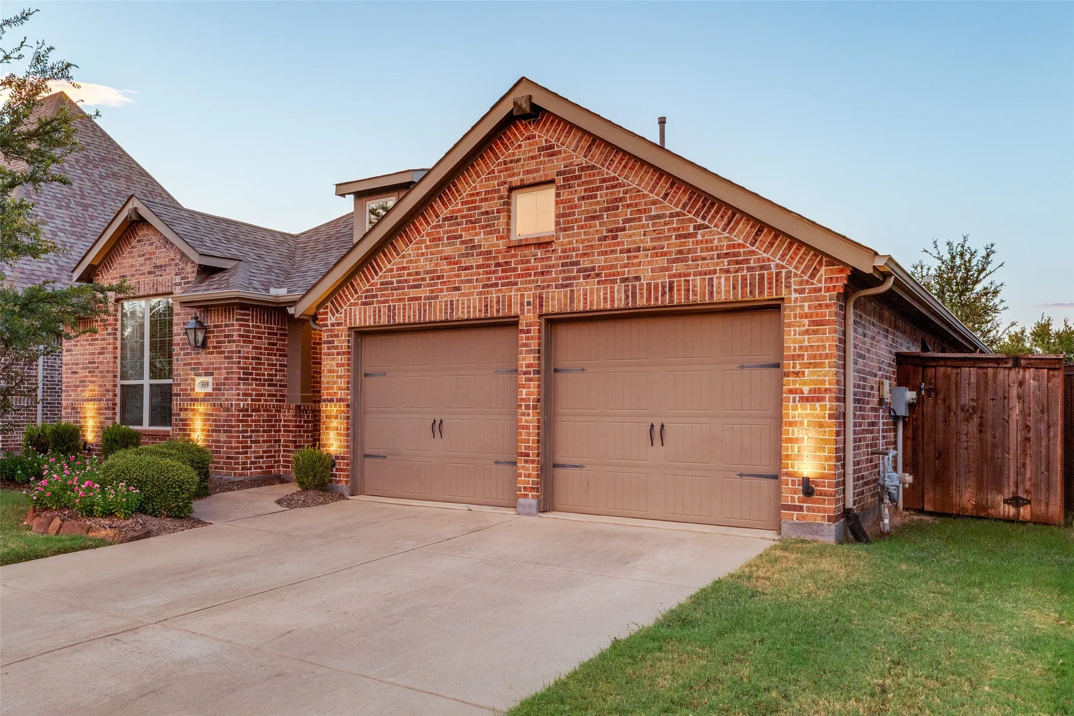 Brick exterior featuring dual garage doors, a concrete driveway, and established landscaping