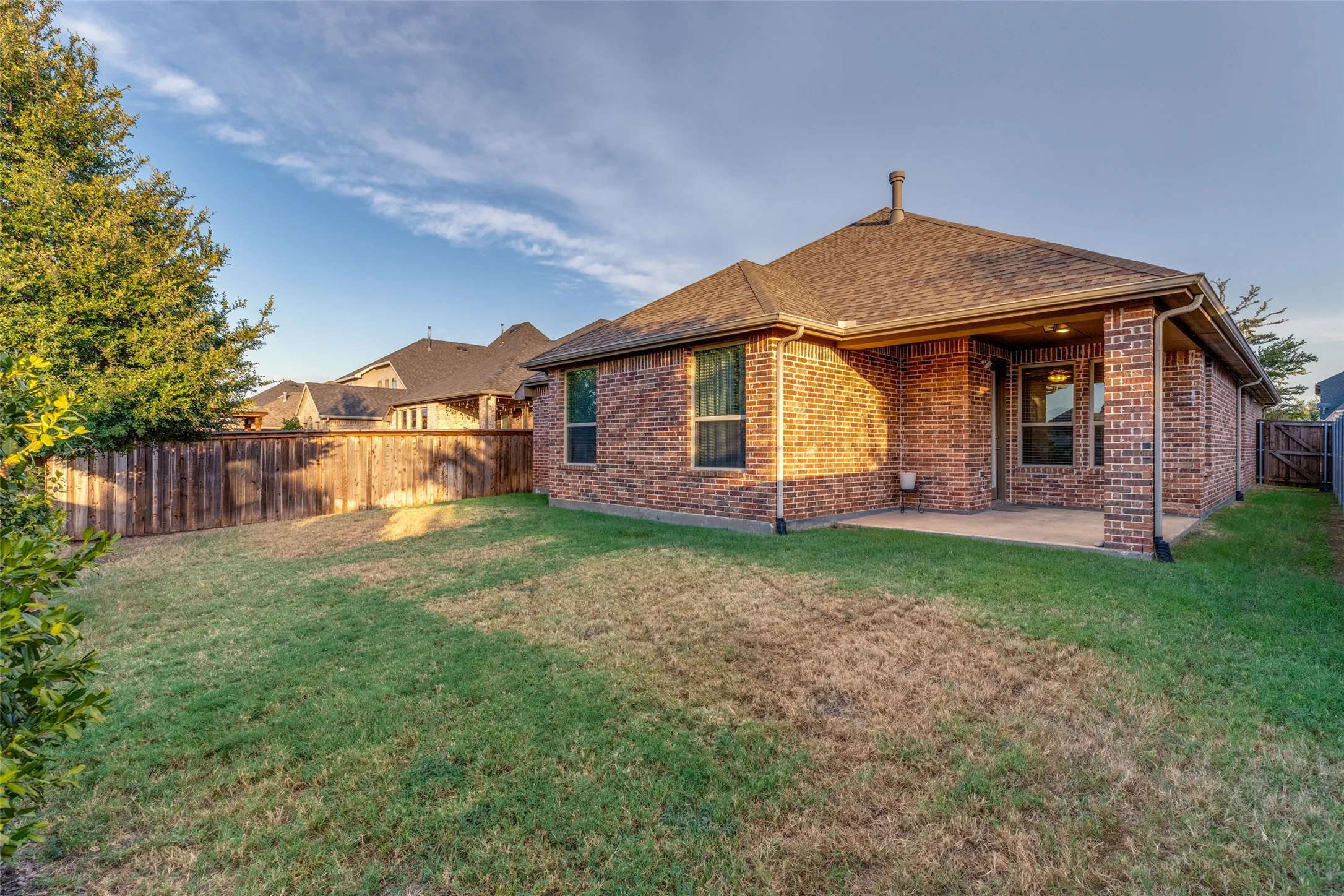 Expansive backyard featuring a wood privacy fence, a covered patio, and a brick exterior