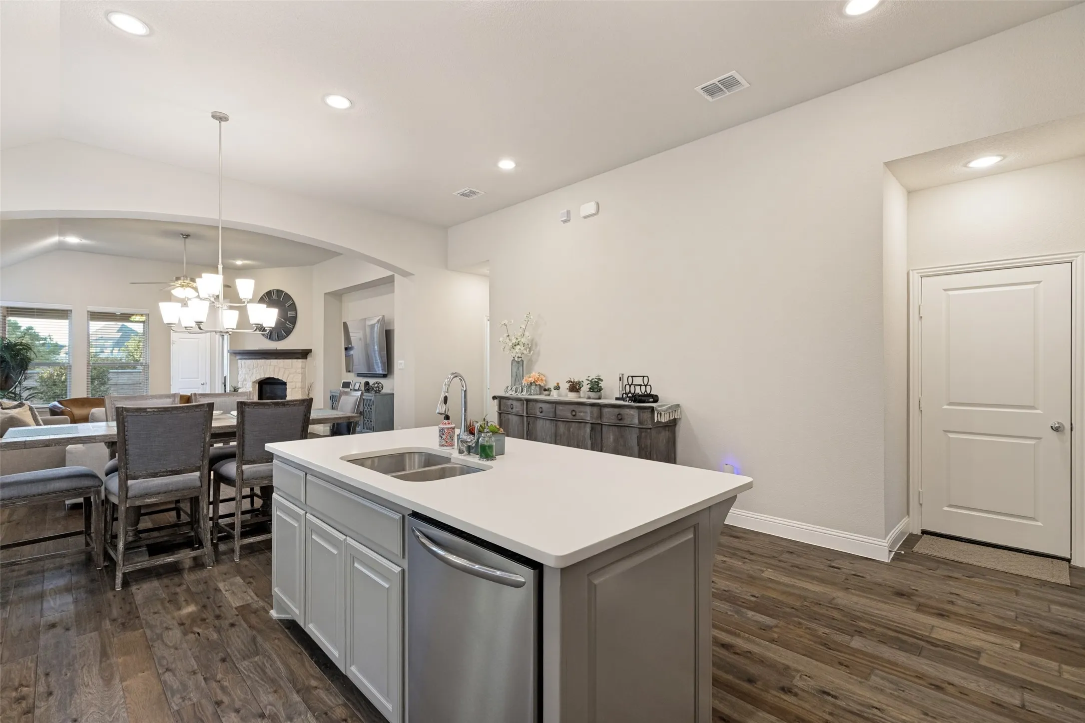 Kitchen island with a white countertop and integrated stainless steel sink, stainless steel dishwasher, wood-finish flooring, recessed lighting, and an arched entryway