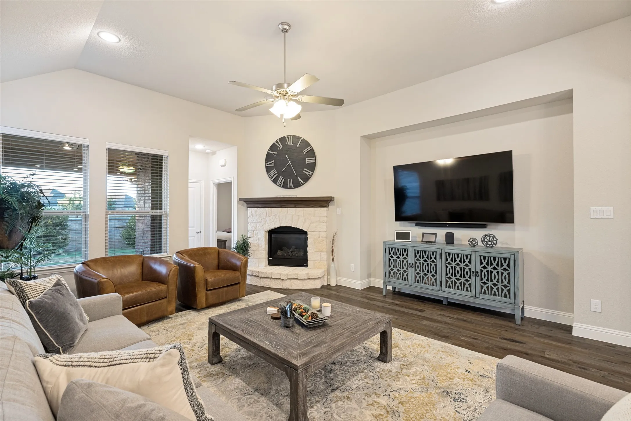 Vaulted ceilings featuring recessed lighting, a stone-faced fireplace with a wood mantle, wood-finish flooring, and lot of windows for light.
