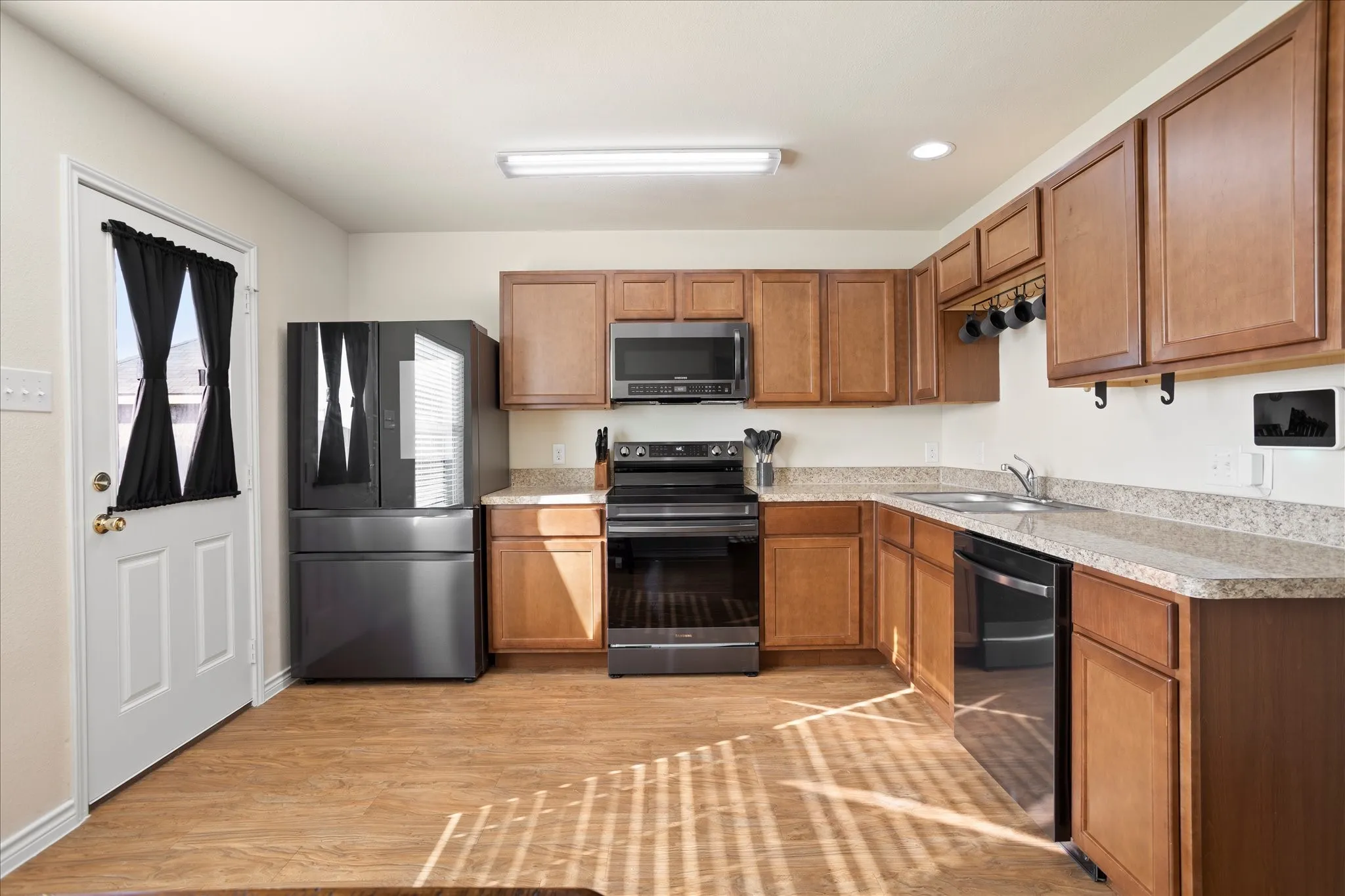Kitchen featuring wood-finish flooring, stone-finish countertops, wood cabinetry, and a full suite of black appliances