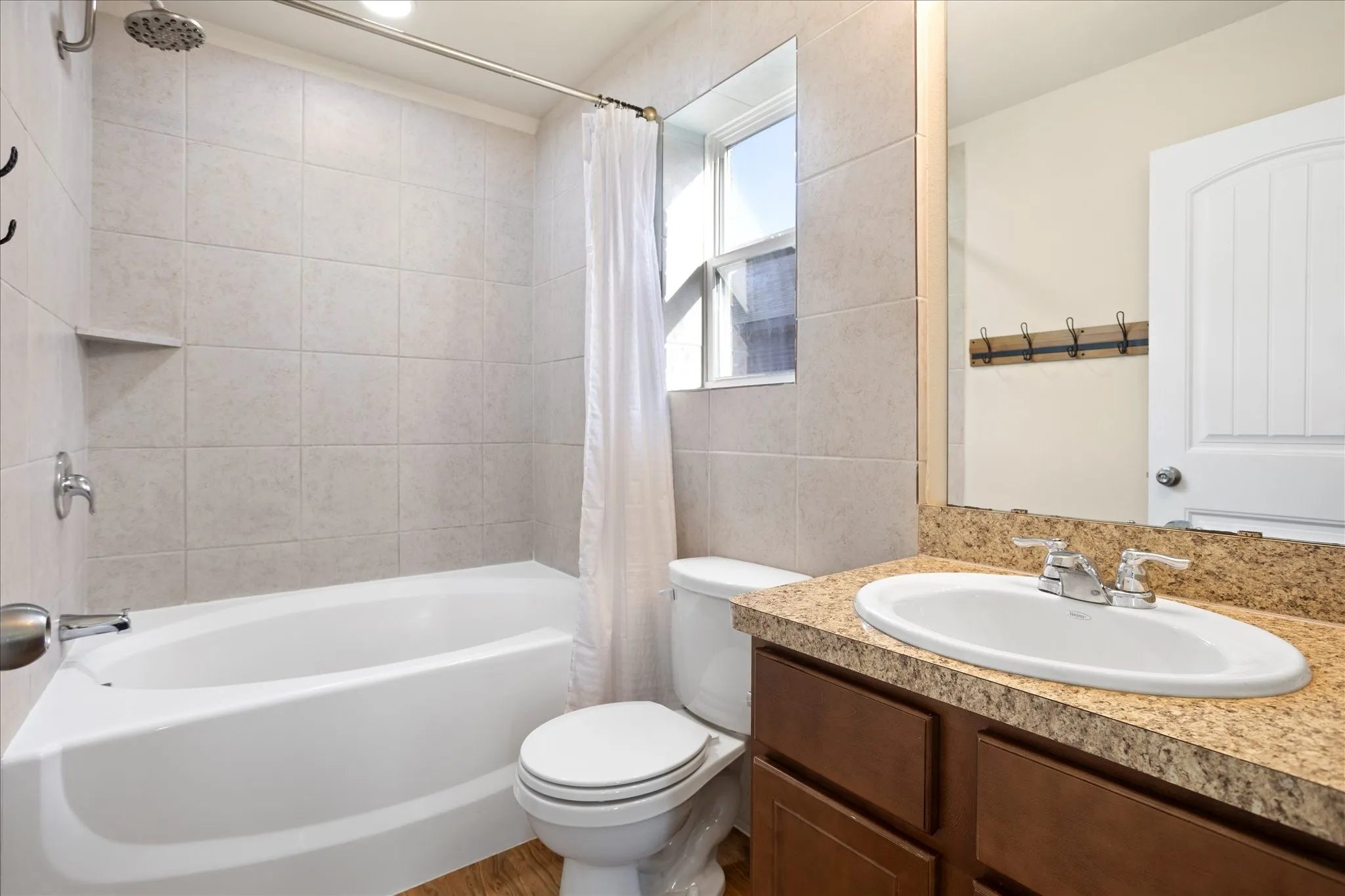 Bathroom featuring a white bathtub, tiled shower surround, recessed shower niche, single-pane window, and a vanity with an integrated sink and wood-finish cabinetry