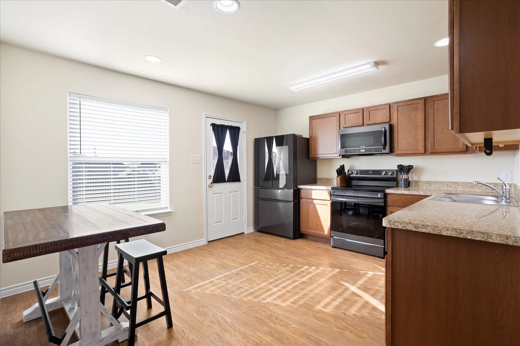 Wood-finish flooring, recessed ceiling lighting, light-toned countertops, wood cabinetry, and a white paneled door