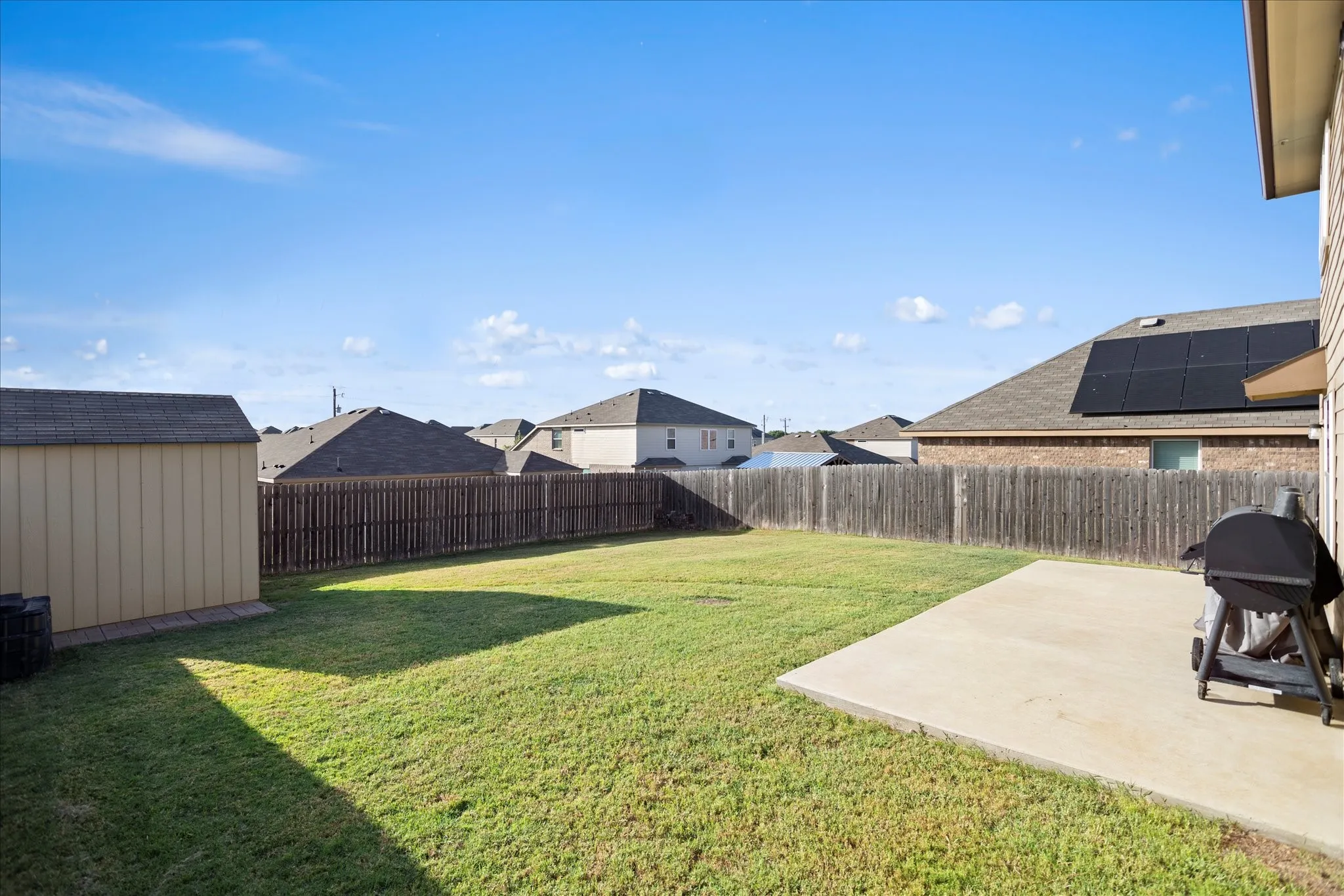Expansive grass lawn with a concrete patio, wood privacy fencing, and an included storage shed