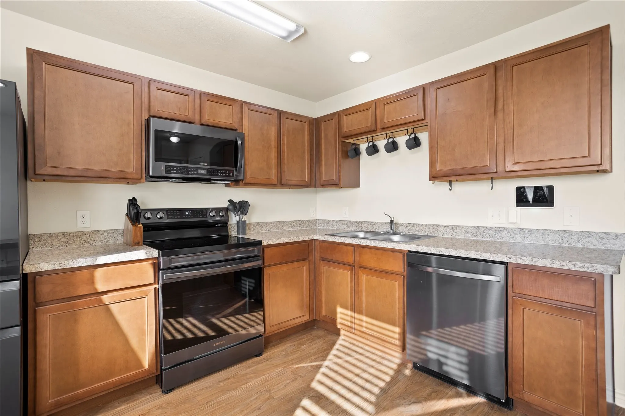 U-shaped kitchen featuring wood-finish cabinetry, light-toned countertops, wood-finish flooring, and stainless steel appliances