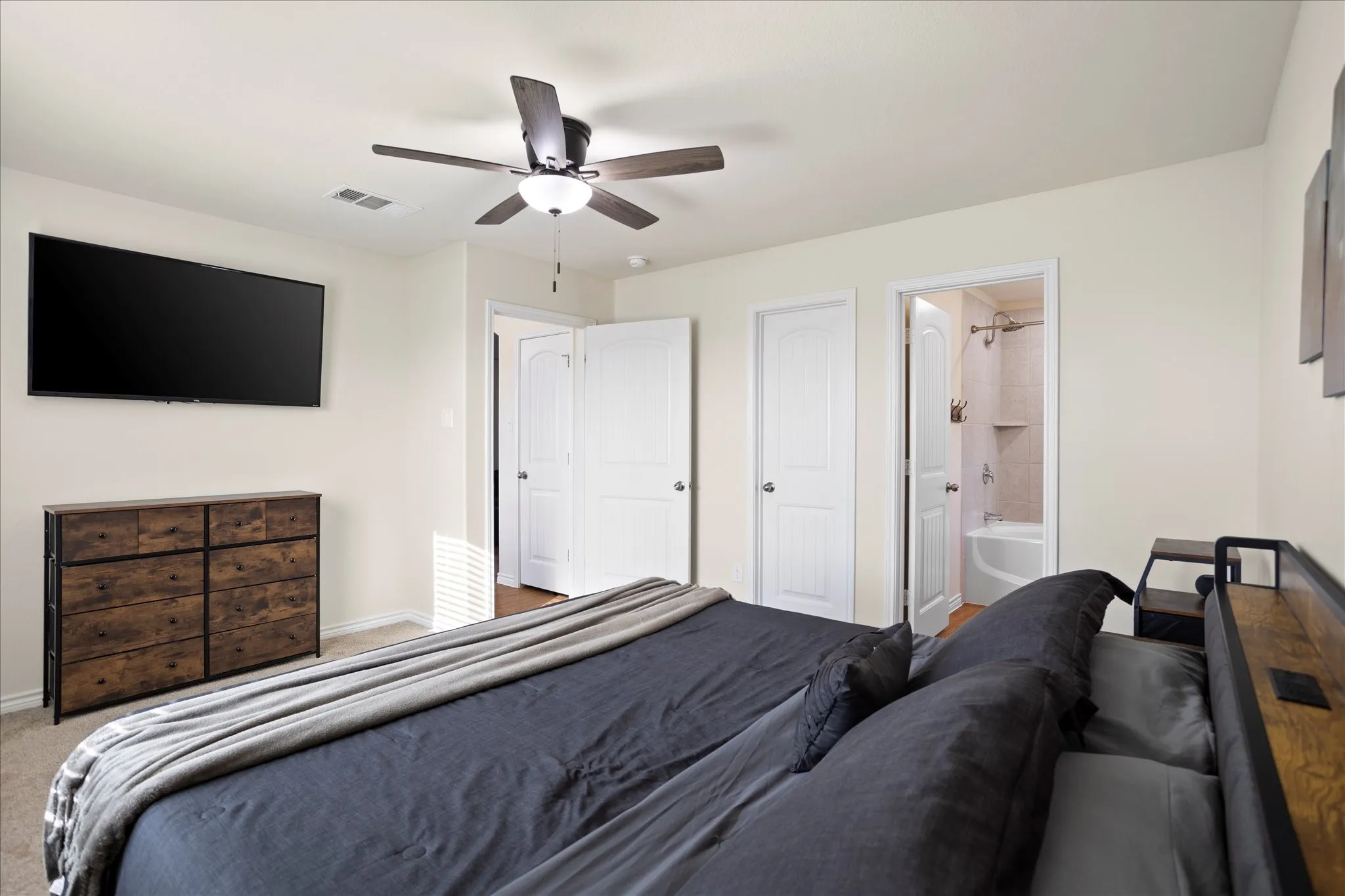 Ceiling fan with integrated lighting, a full bathroom with a tiled tub surround, and a white paneled door