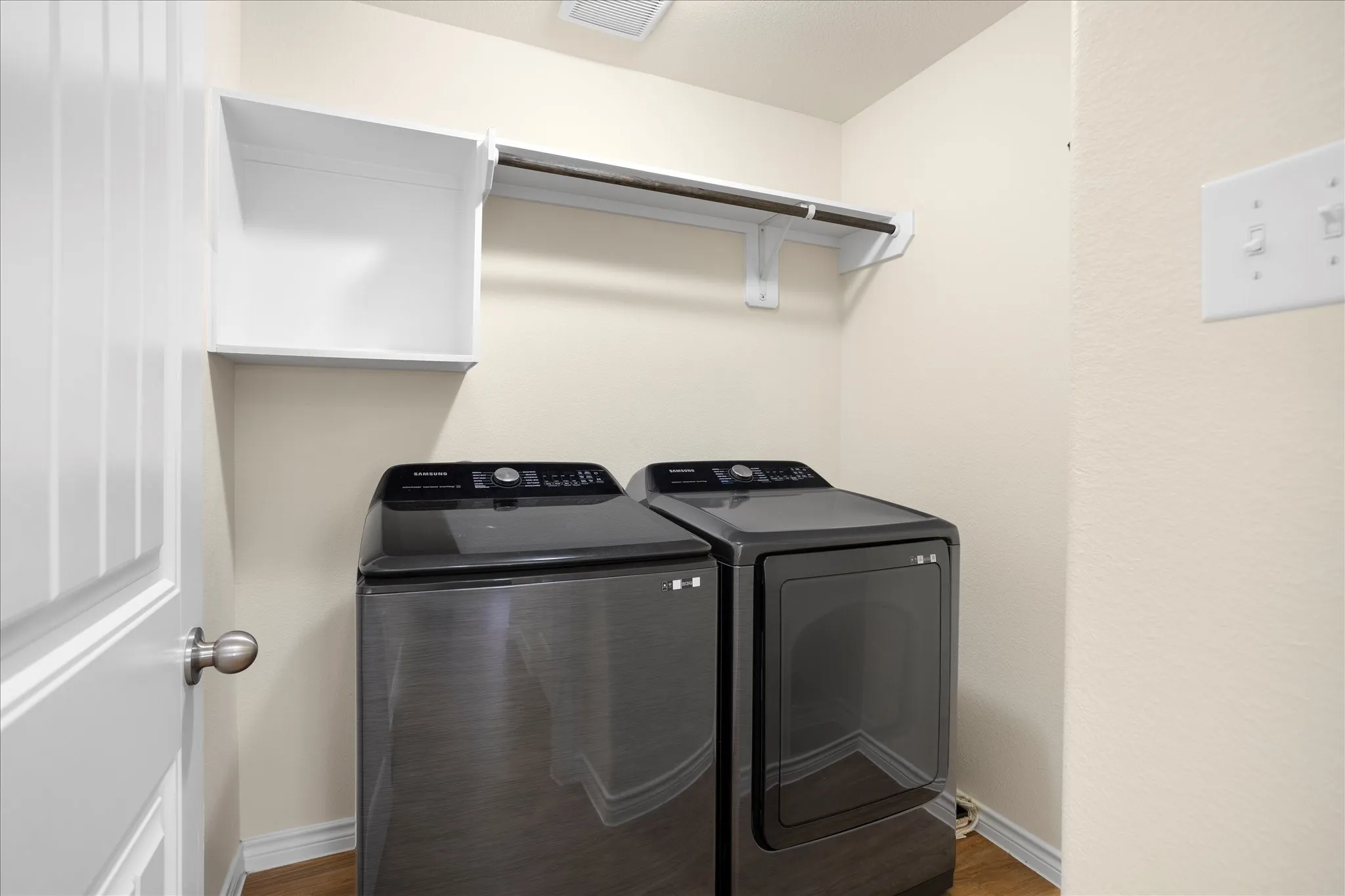 Utility area featuring a wall-mounted shelf, hanging rod, and wood-finish flooring