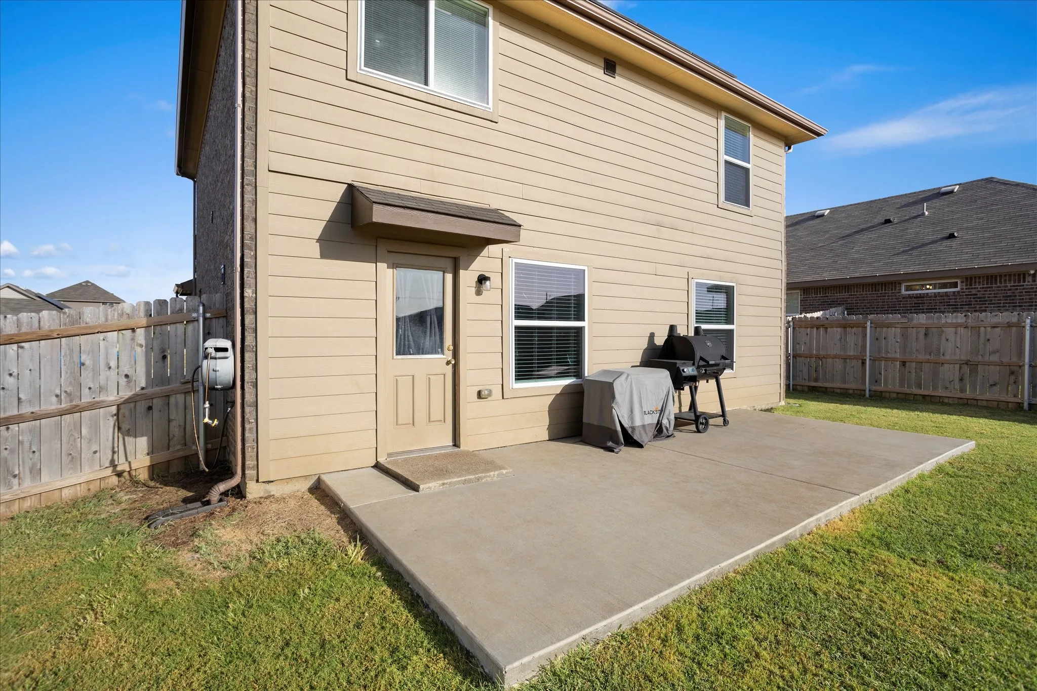Expansive concrete patio, wood-paneled siding exterior, brick accent wall, privacy fencing, and upper-level windows