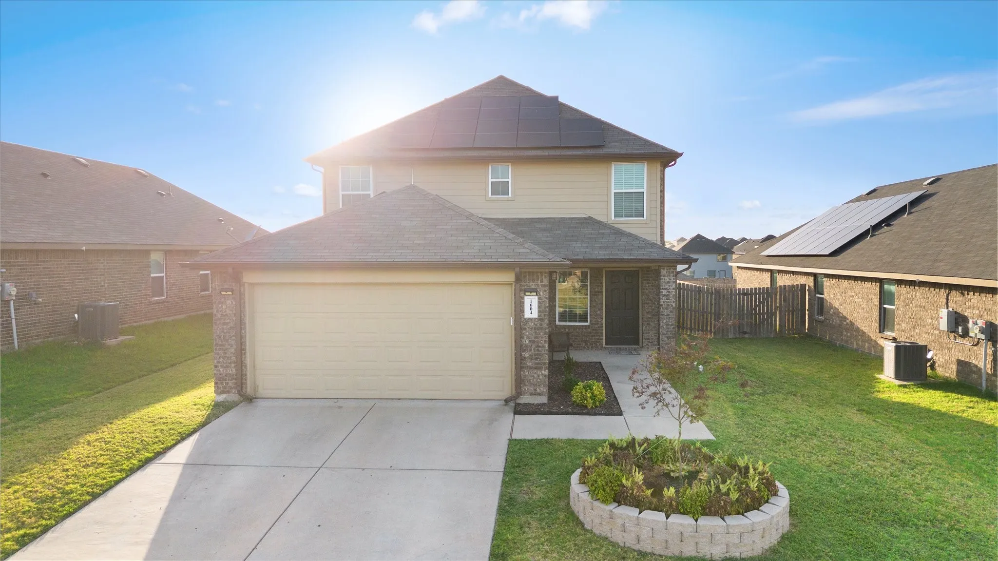 Two-story residence featuring a two-car garage, brick and siding exterior, solar panels, and a concrete driveway