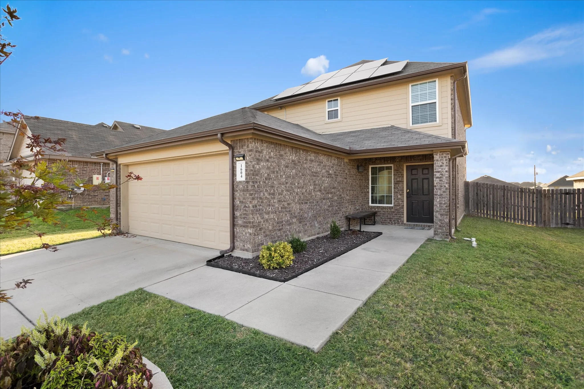 Two-story exterior featuring brick and siding finishes, an attached garage, a covered entry, and solar panels