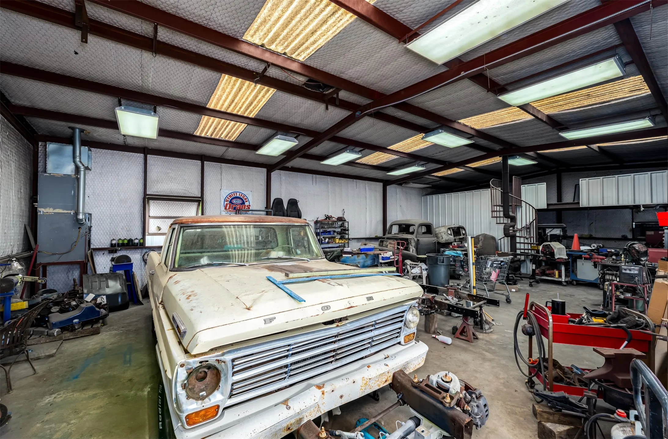 Spacious workshop featuring a metal beam structure, corrugated metal roof panels, fluorescent lighting, and a spiral staircase
