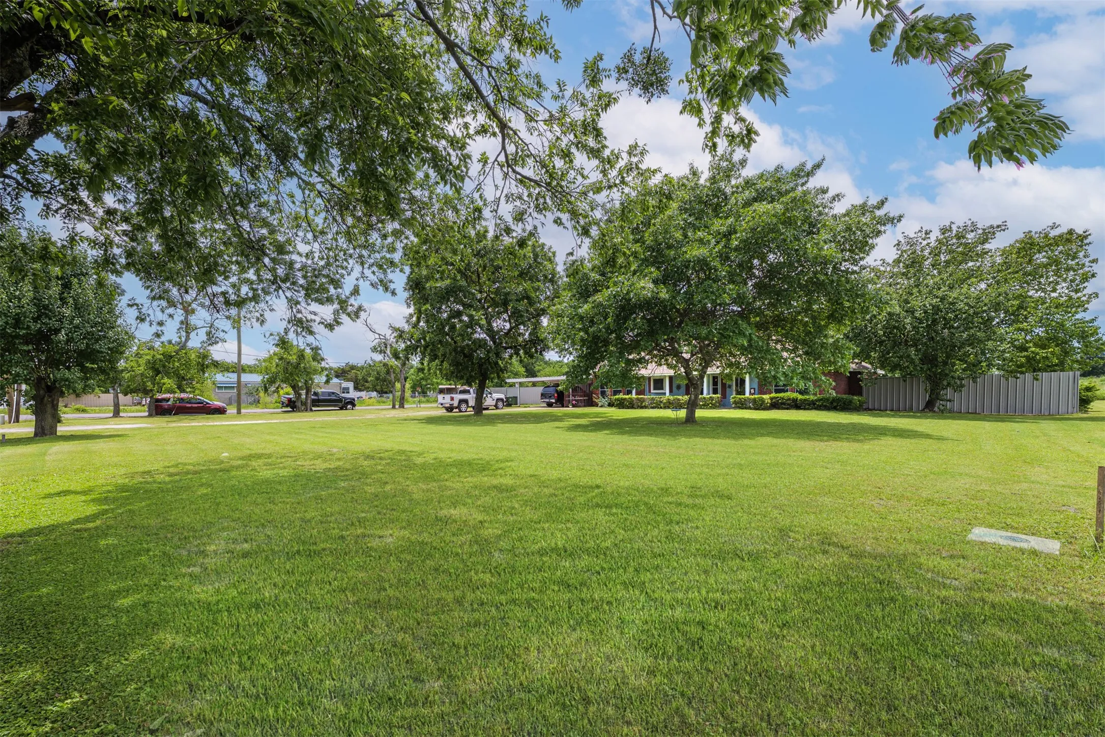 Expansive green lawn with mature trees and partial fencing