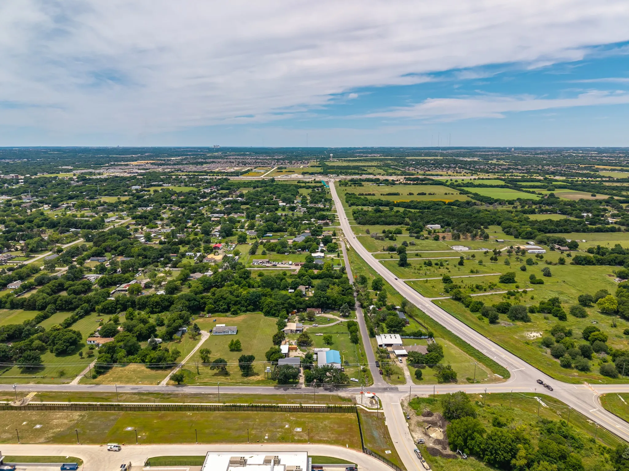 Expansive land parcels with scattered trees, bordered by a multi-lane road and residential areas