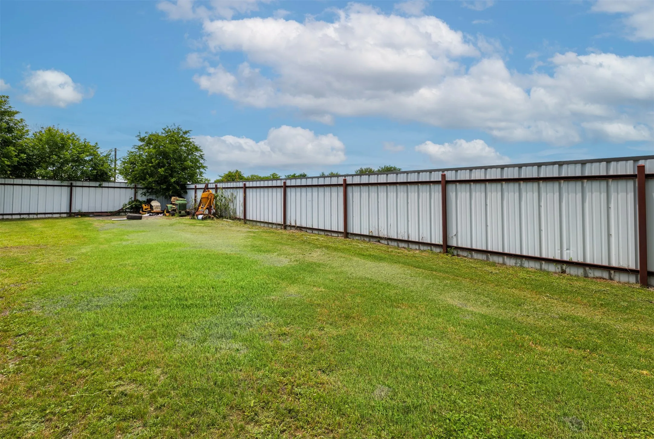 Expansive green space featuring a corrugated metal fence with visible posts
