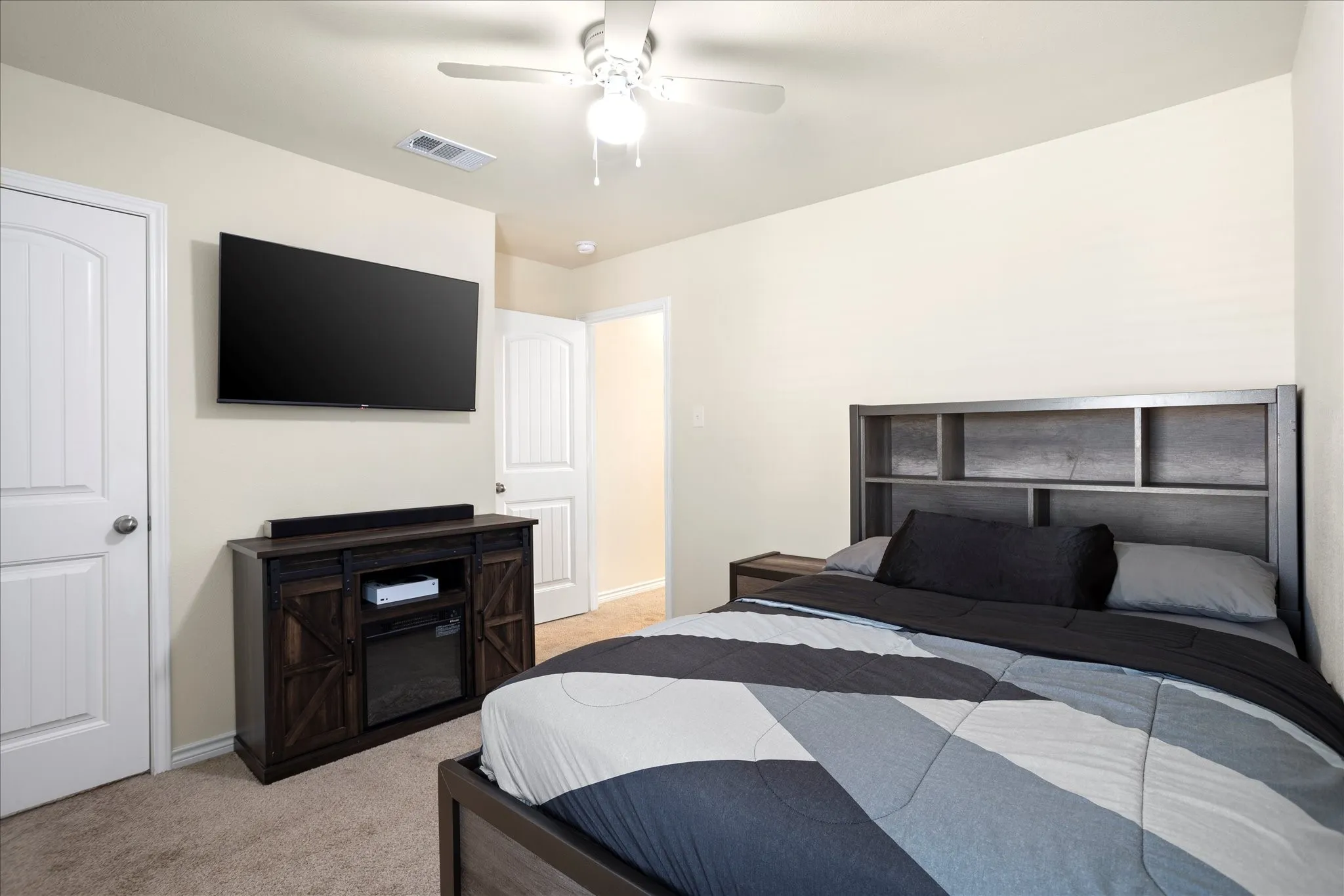 Carpeted bedroom featuring a ceiling fan with integrated lighting, two paneled doors, and an entertainment console with a built-in electric fireplace