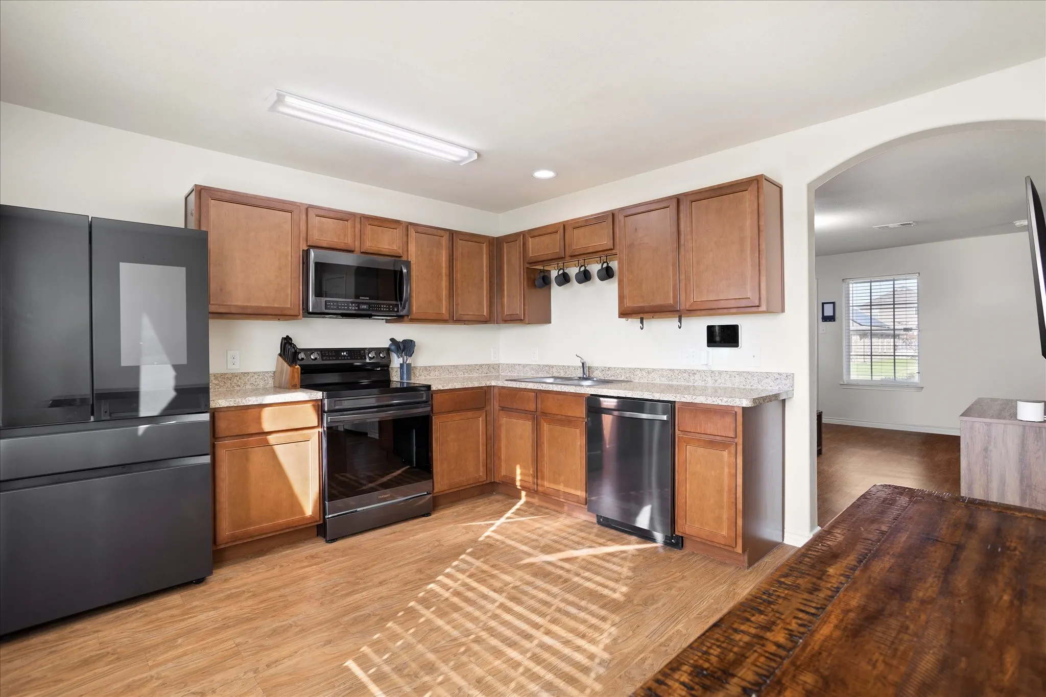 Kitchen featuring wood-finish flooring, a full suite of black and stainless steel appliances, light-colored countertops, and wood cabinetry