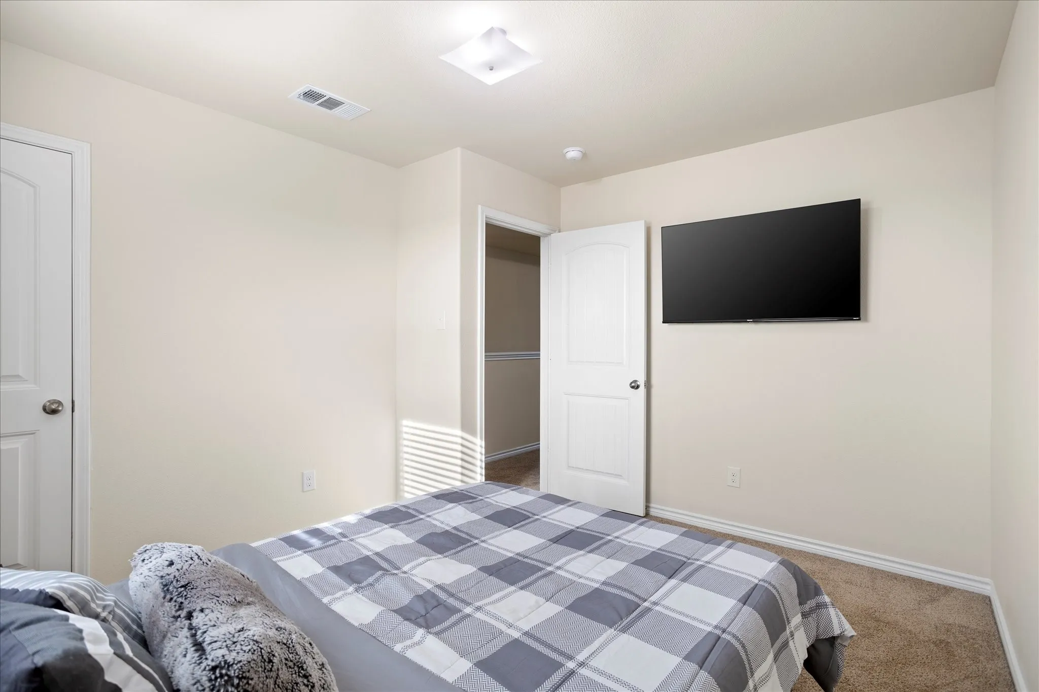 Carpeted bedroom with a built-in wall-mounted television and a flush-mount ceiling light