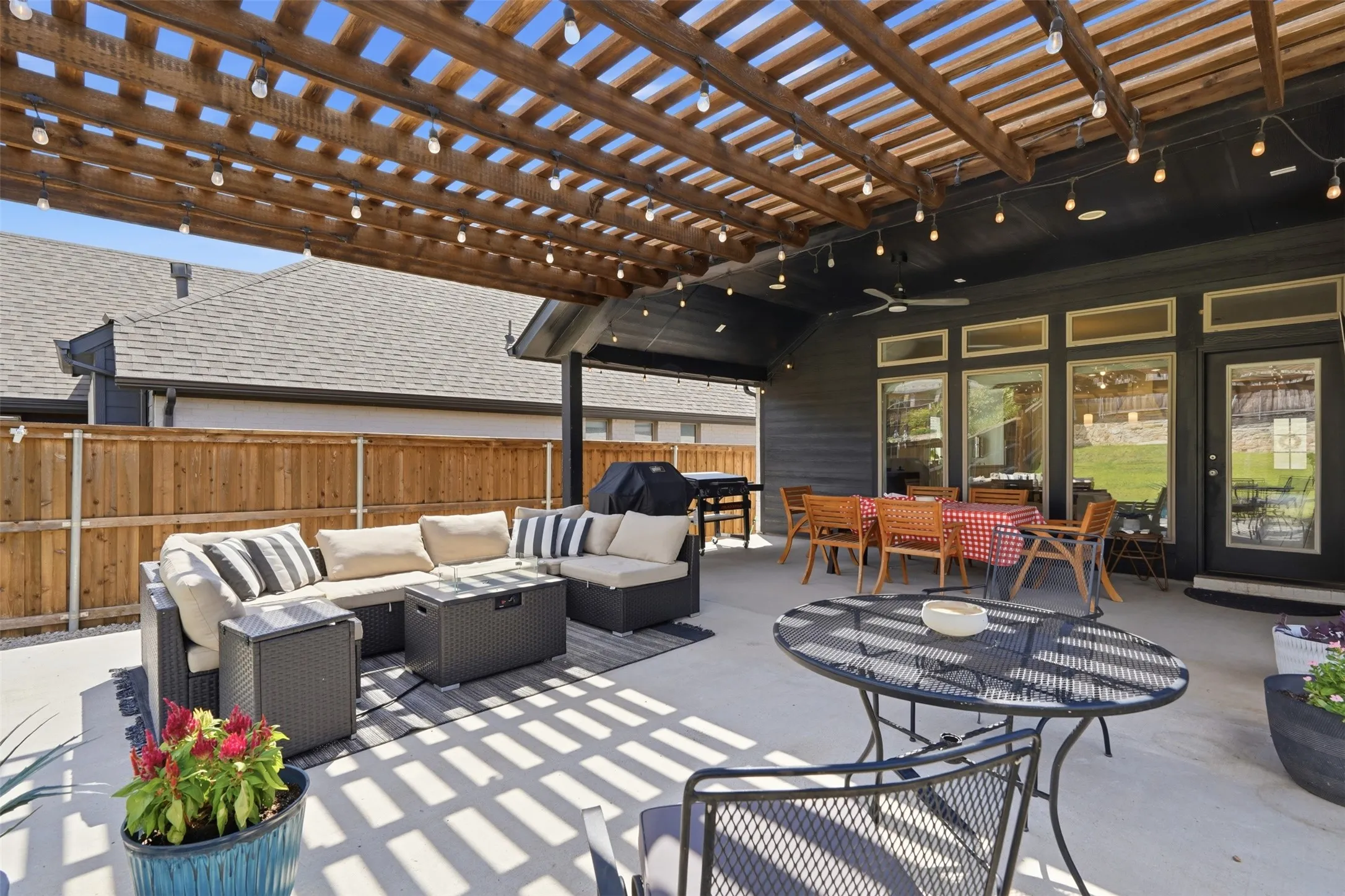 Expansive patio featuring a wood pergola with string lighting, concrete flooring, and a dark-paneled exterior