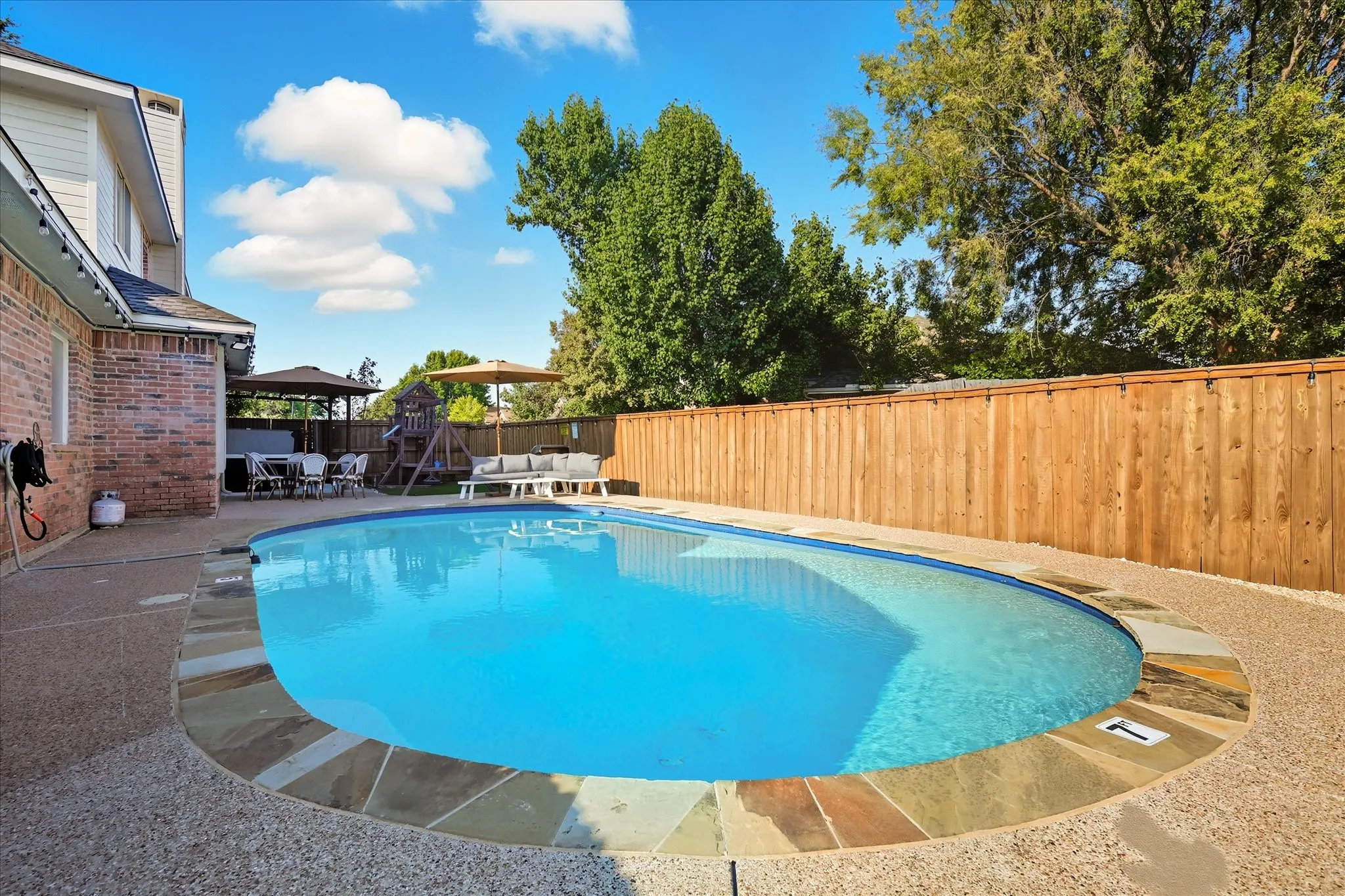 Oval-shaped swimming pool with stone coping, textured concrete decking, and a wood privacy fence