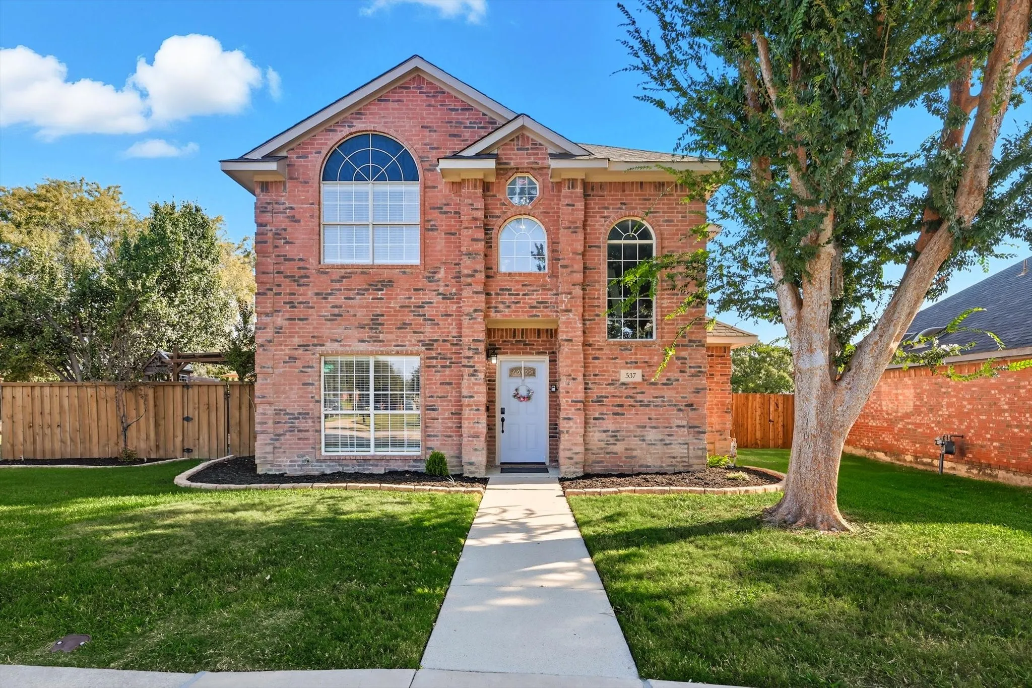 Two-story brick exterior with arched windows, a white front door, and a concrete pathway