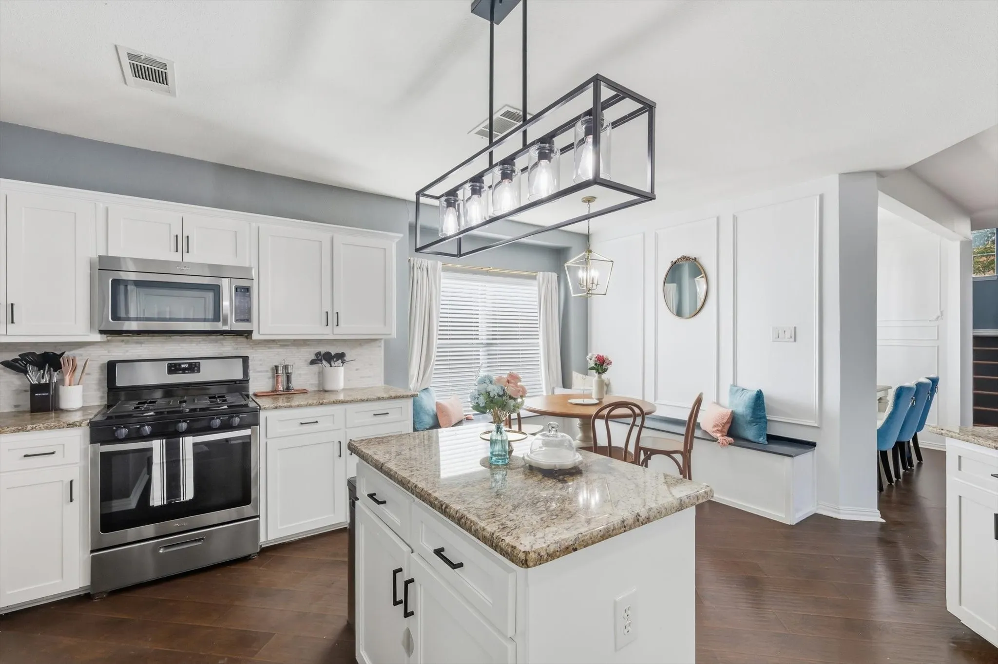 White cabinetry with black hardware, stainless steel range and microwave, light-toned backsplash, granite countertops, and wood-finish flooring