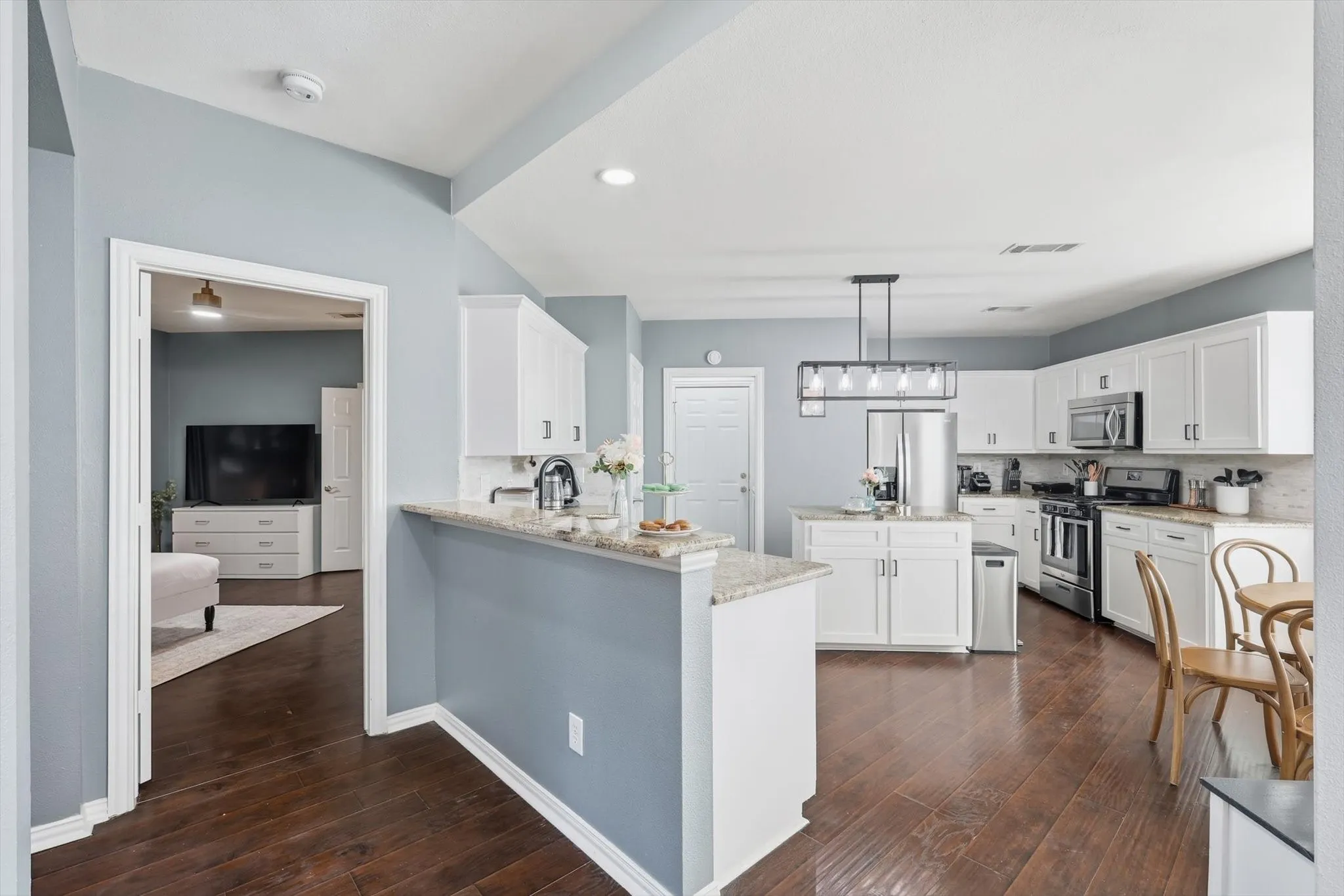 Kitchen featuring white shaker cabinetry, stainless steel appliances, a center island with countertop seating, and wood-finish flooring