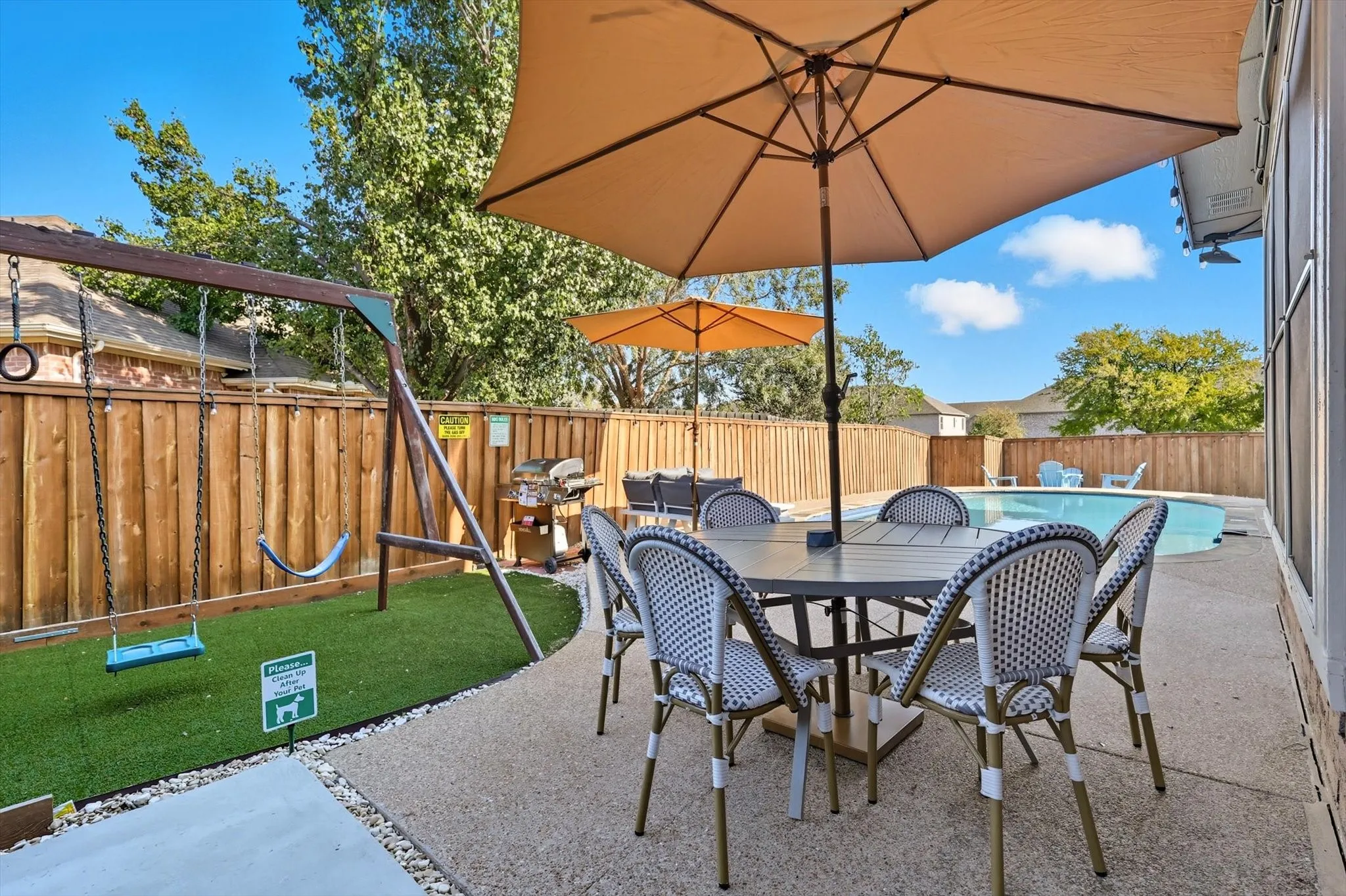 Concrete patio with an inground pool, wood privacy fencing, and artificial turf