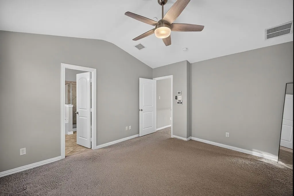 Vaulted ceiling with an attached ceiling fan and light fixture, neutral grey wall paint, and brown carpet flooring