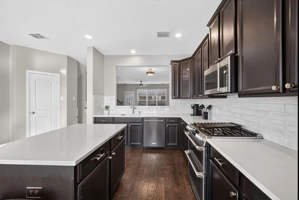 Spacious kitchen featuring dark wood cabinetry, light-toned countertops, and stainless steel appliances including a gas range and built-in microwave