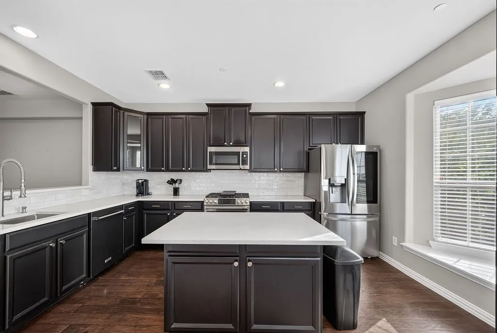 Kitchen featuring dark wood-finish cabinetry, white countertops, white subway tile backsplash, and stainless steel appliances