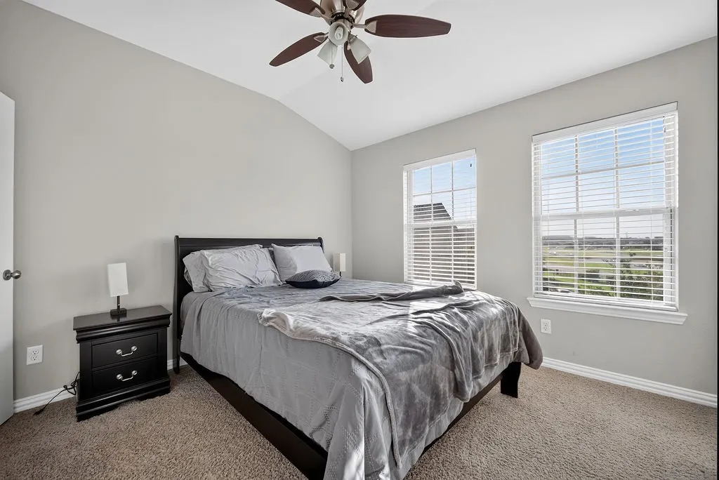 Vaulted ceiling with a ceiling fan, two double-hung windows with blinds, and soft carpet flooring