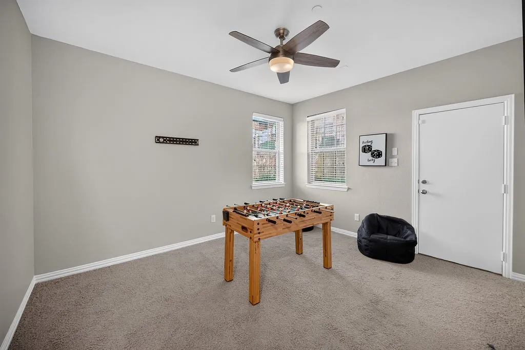 Neutral-toned carpeting, ceiling fan with integrated lighting, two windows with blinds, and a white door with brushed nickel hardware